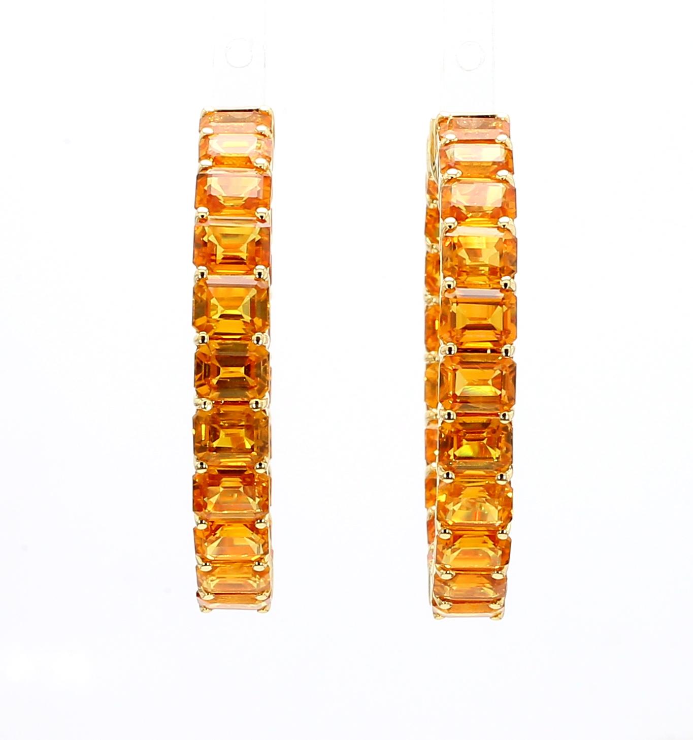 These 18K yellow gold hoop earrings with emerald-cut heated yellow sapphire stones, measuring around 1.25 inches in diameter, are a fashionable and easy-to-wear accessory. The bright orange-yellow color of the approximately 22.76 carats of yellow