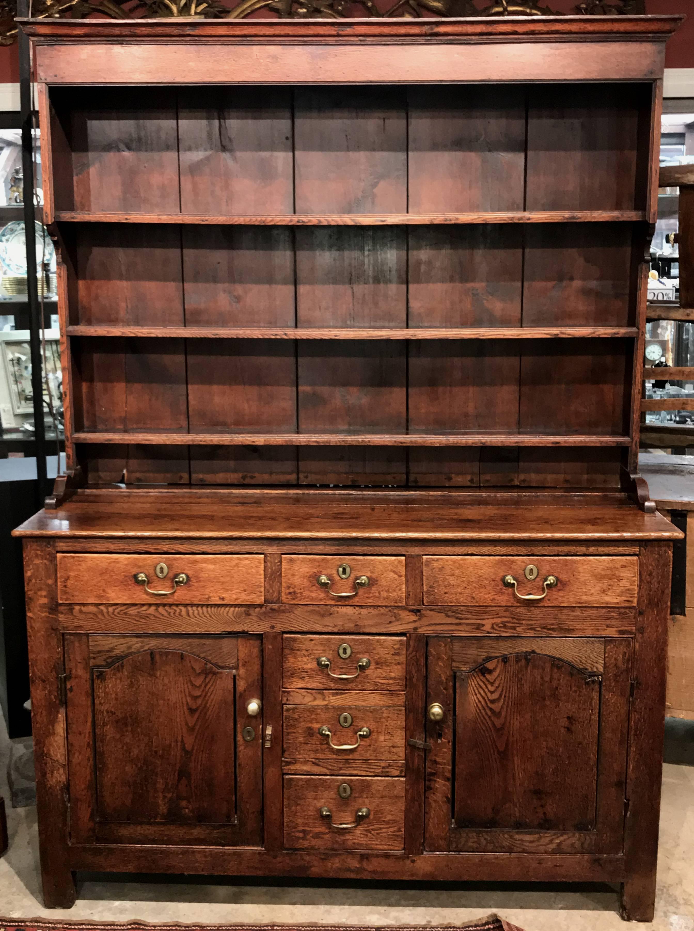 A fine two-part George III Welsh two-part dresser or cupboard in oak, its bookcase top case with molded cornice over three open shelves, supported by shoe feet, surmounting a rectangular lower case with three fitted drawers over three vertical