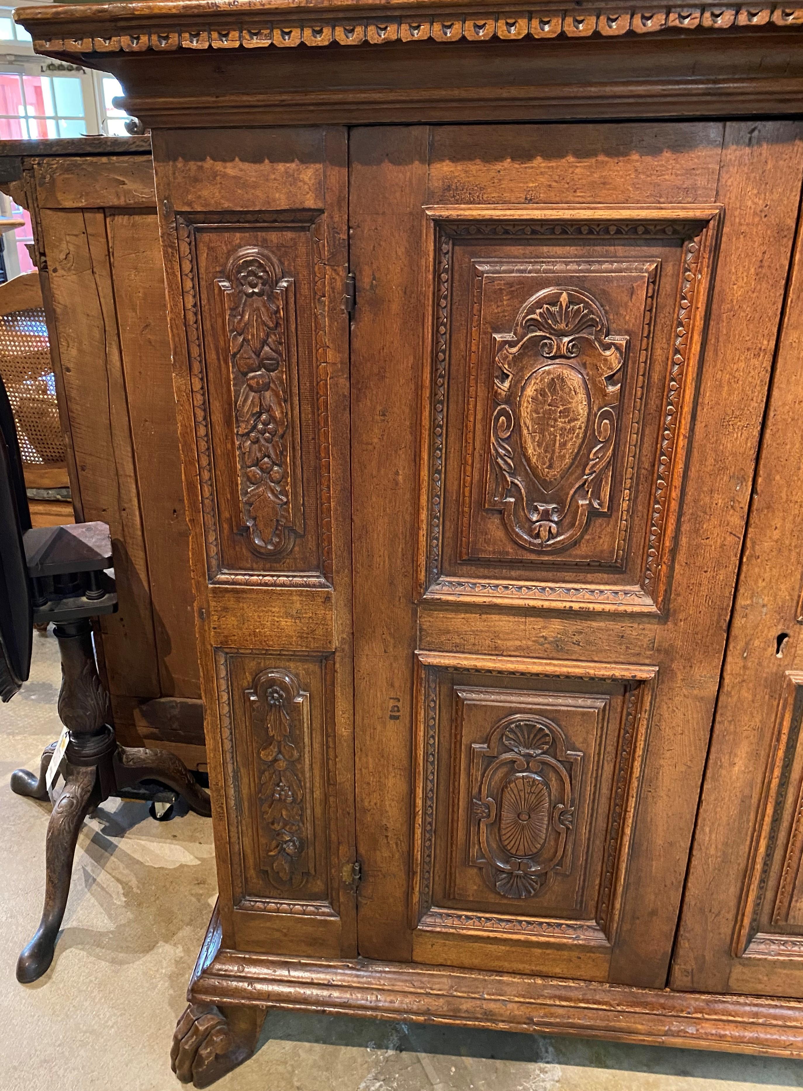 A fine example of a large Italian Baroque style carved oak cabinet with molded cornice featuring dentil molding surmounting a case with two doors featuring raised relief carved foliate panels, which open to an interior two shelf compartment, flanked