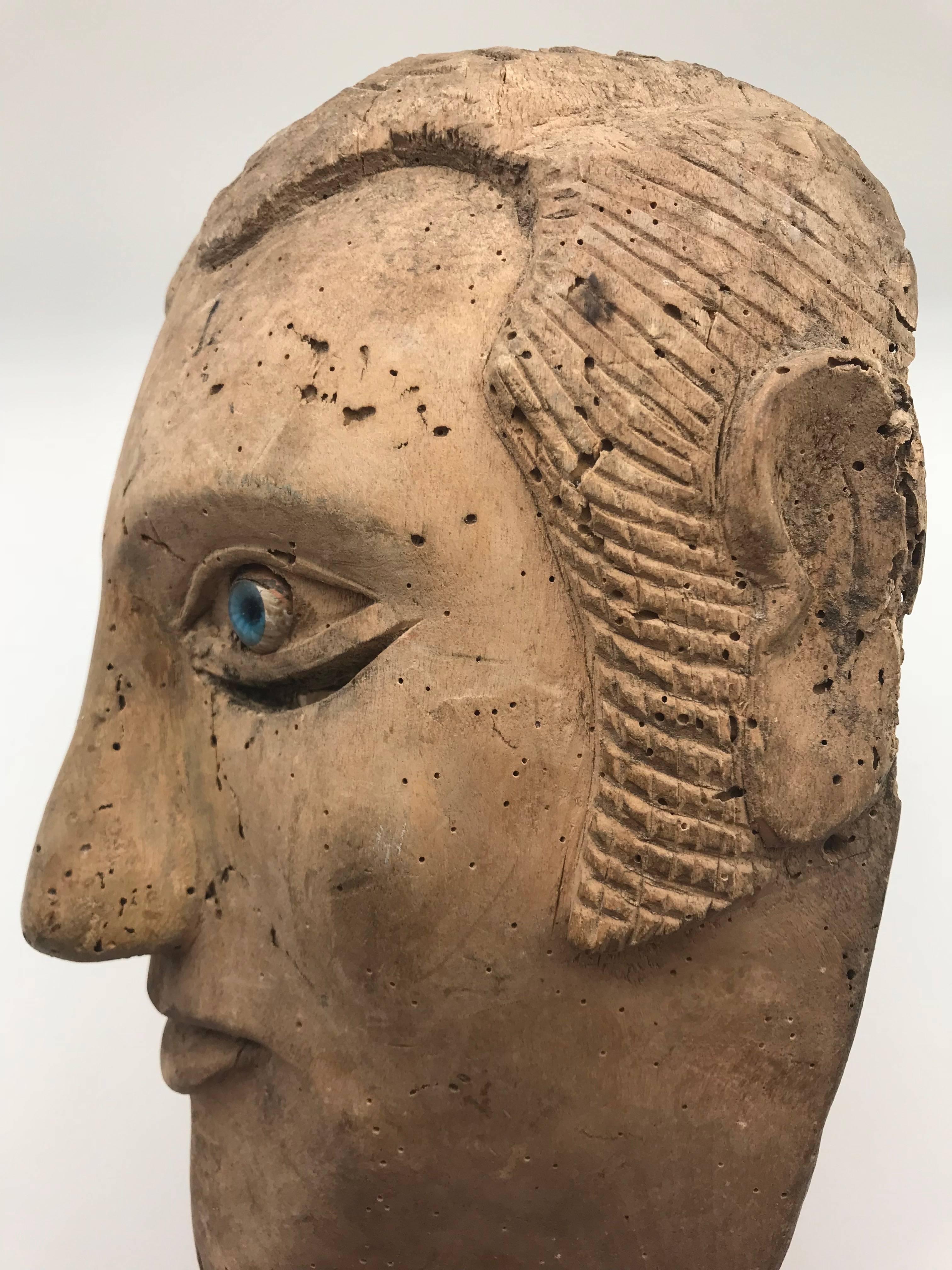 Unique carved mask made by a slave, depicting his or her master. Over enhanced facial features are apparent while blue glass eyes distract from the slits where the user would see through.