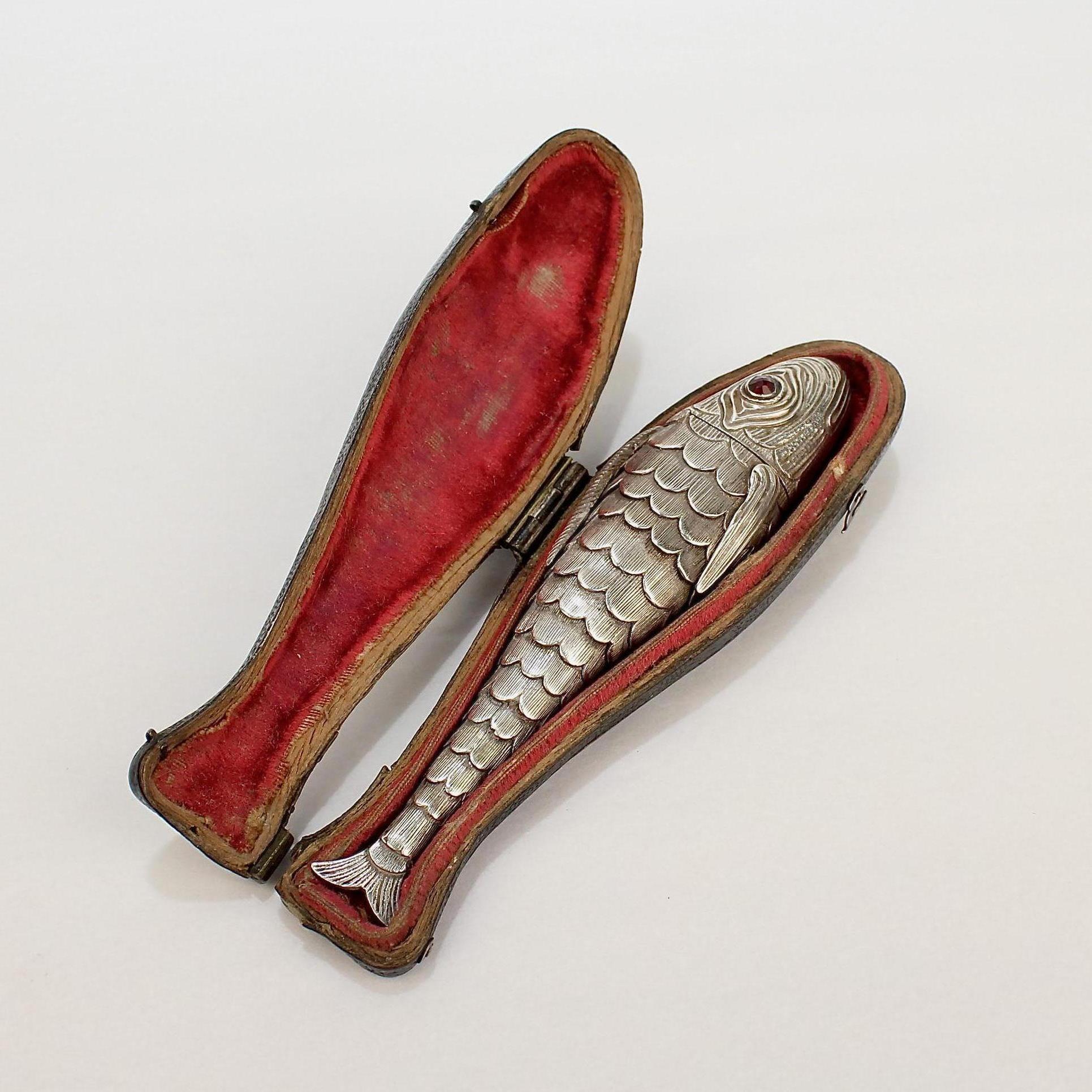 A very fine solid silver antique figural vinaigrette.

In the form of a fish with faceted garnet gemstone eyes and engraved fins and scales.

Its hinged cover in the form of the fish's head opens to reveal a sponge compartment. The body supports 7