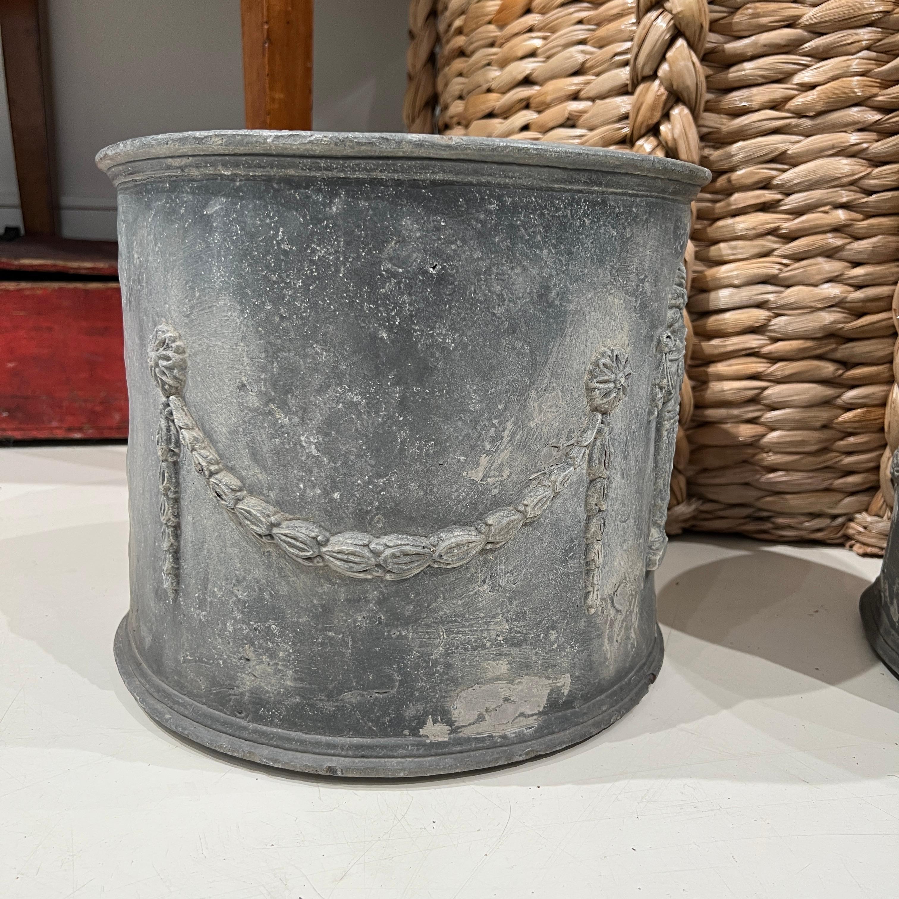 A classic pair of English lead planters adorned with elegant garland reliefs and amphoraae showcasing timeless craftsmanship and weathered patina—ideal for adding a touch of stately charm to garden or terrace settings.
