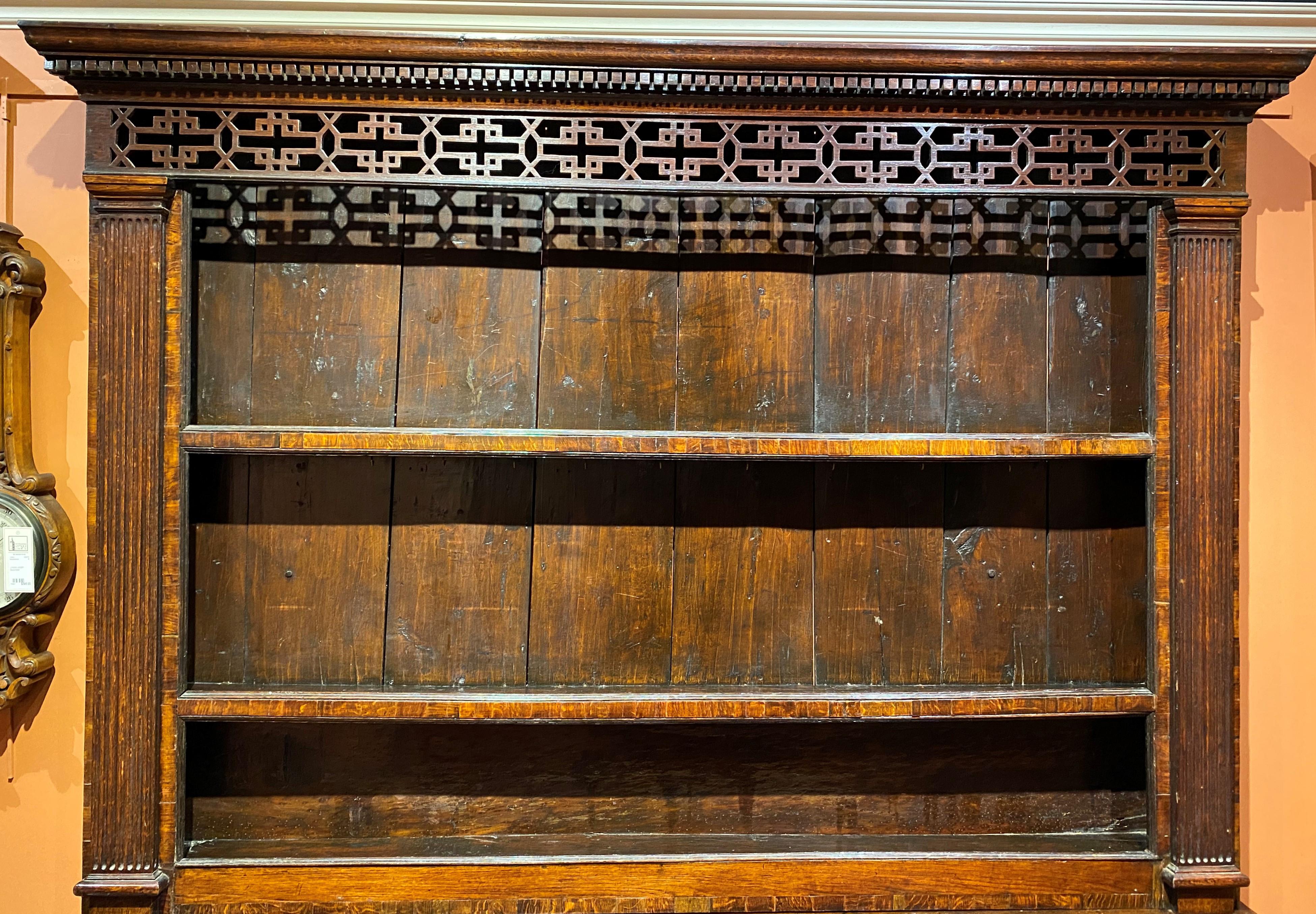 A fine example of a two part English Welsh oak cupboard or dresser, its upper case with an molded cornice featuring dentil molding and reticulated carved front top decoration, surmounting two open plate shelves flanked by reeded flat support