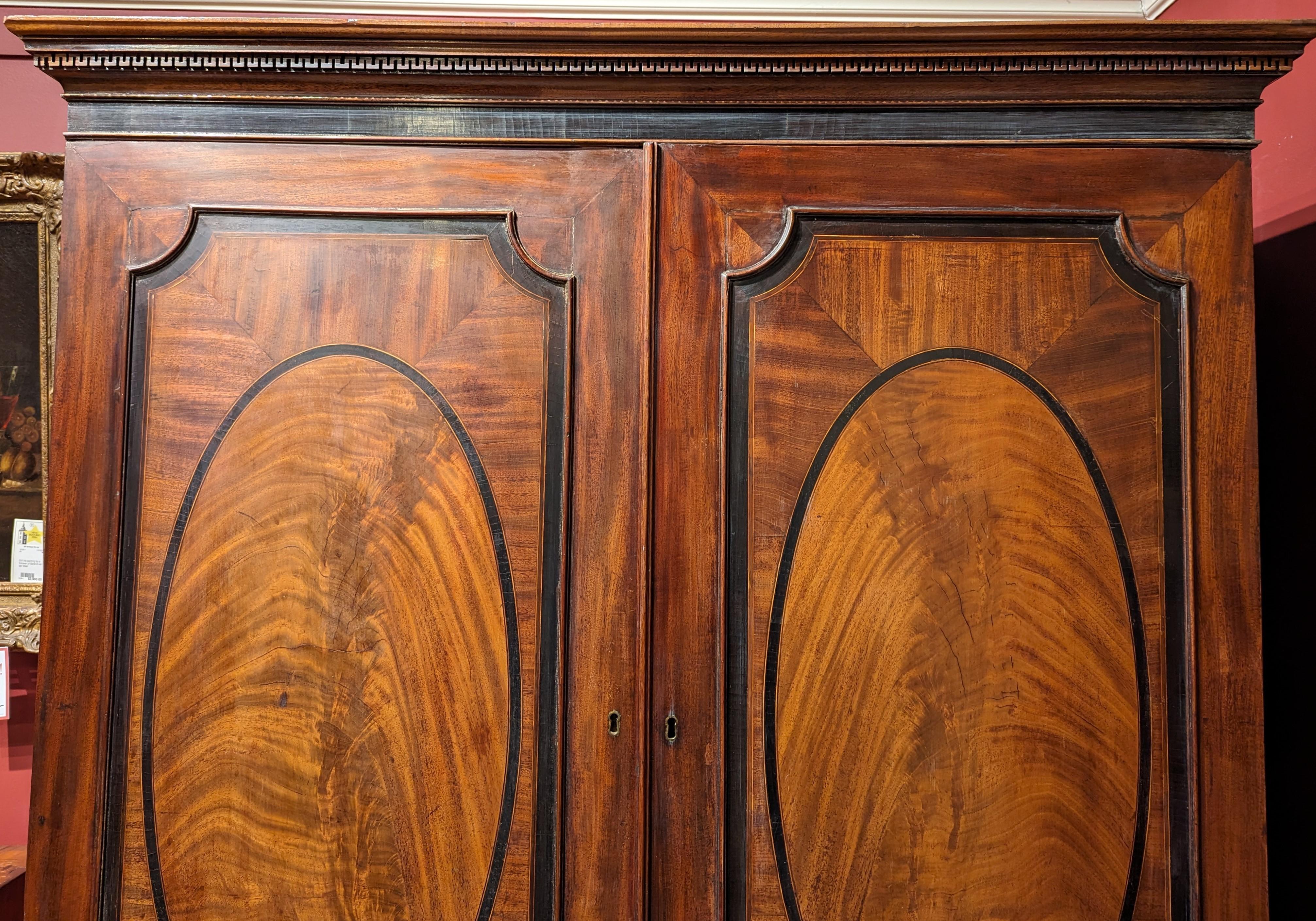 A large Georgian mahogany two door linen press with a molded cornice with Greek key motif surmounting two large doors, opening to an interior storage with an adjustable slide out linen shelf, with four fitted lower drawers below. The front paneled