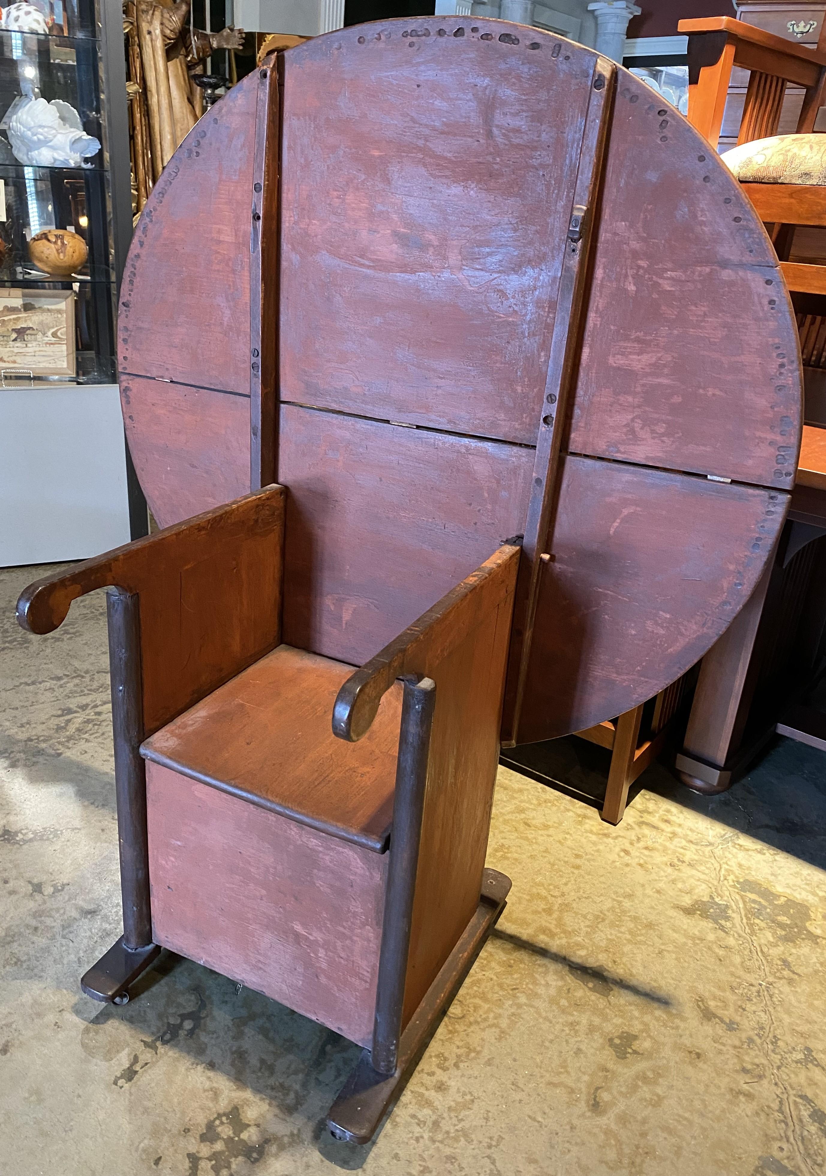 A fabulous example of a late 18th or early 19th century American round hutch or chair table in old red surface, with great patina, wooden pegs, original seat hinges, evidence of sewing bird clamps underneath table top earlier, and later added