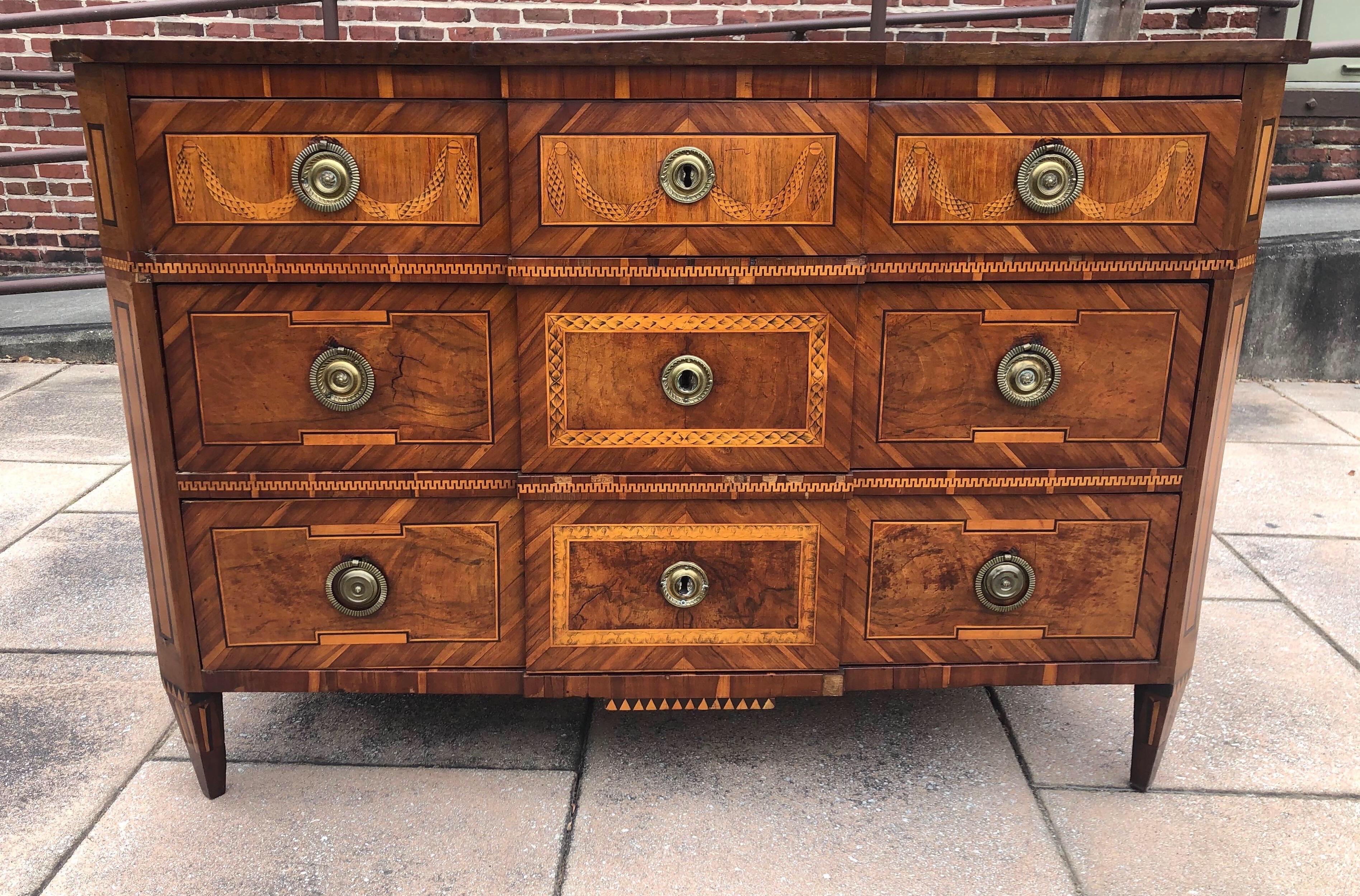 Gorgeous color on this 18th-19th century Italian neoclassical inlaid commode. Stout three drawer commode with navigational rose on the top and swags/tassels on the sides and top drawer faces. Crossbanding and geometric motifs inlaid throughout.