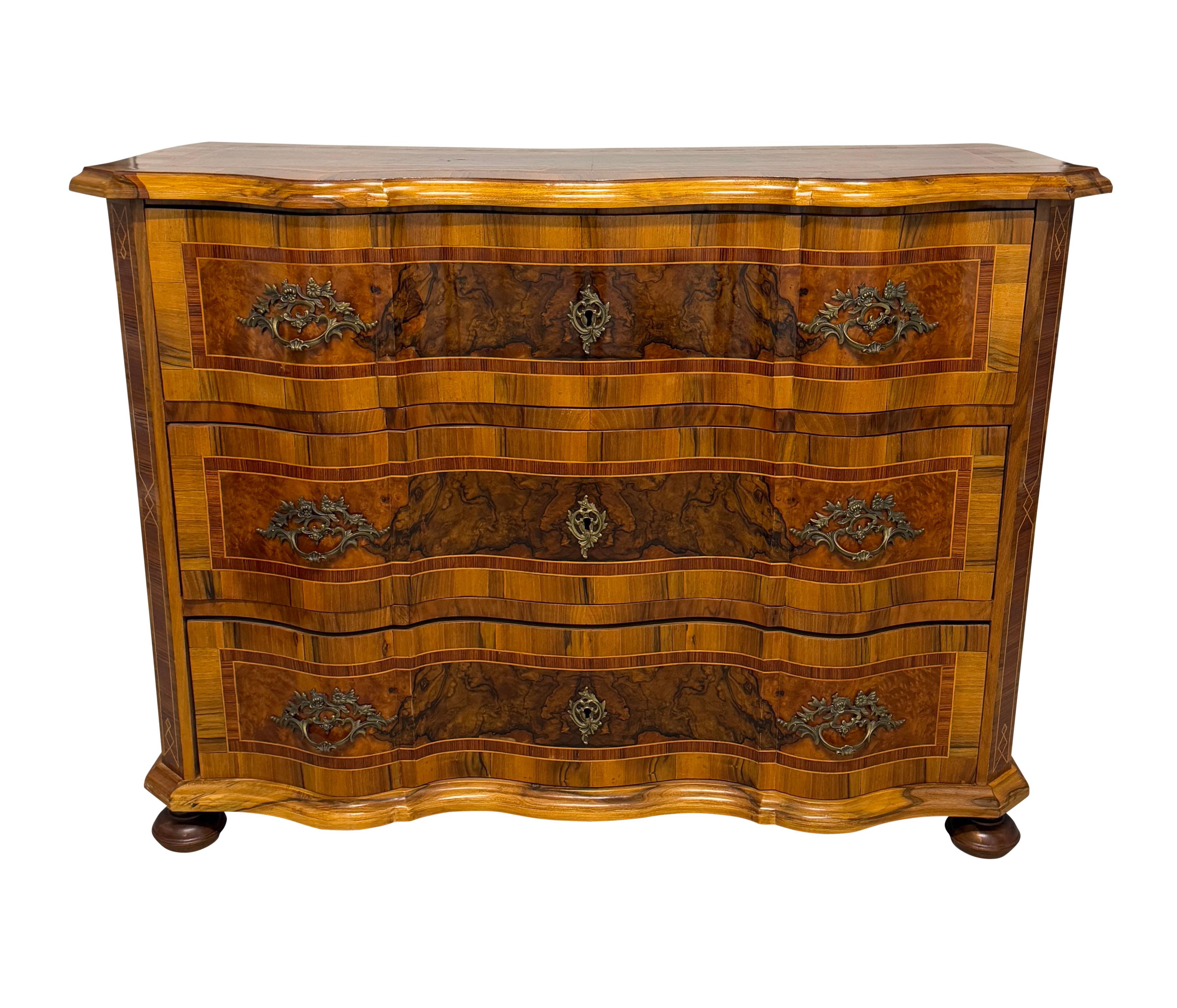 Una cassettiera barocca dell'Italia settentrionale dei primi del XIX secolo. Commodo italiano a 3 cassetti in noce a serpentina con intarsio in parquet e piedini a baldacchino. Colore e patina meravigliosi. 
La commode presenta splendidi motivi di
