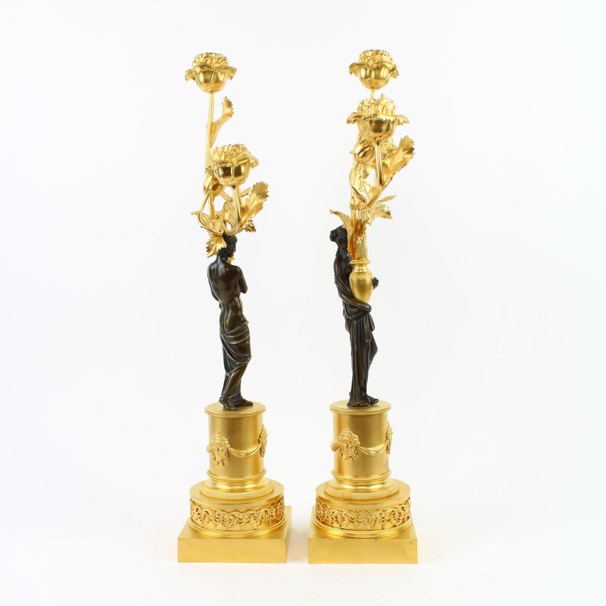 Pair of end of 18th/early 19th century Russian neoclassical figural gilt and patinated bronze candelabra.

Gilt-bronze circular pedestal on rectangular plinth, the base with neoclassical foliate frieze, the pedestal with surrounding frieze of