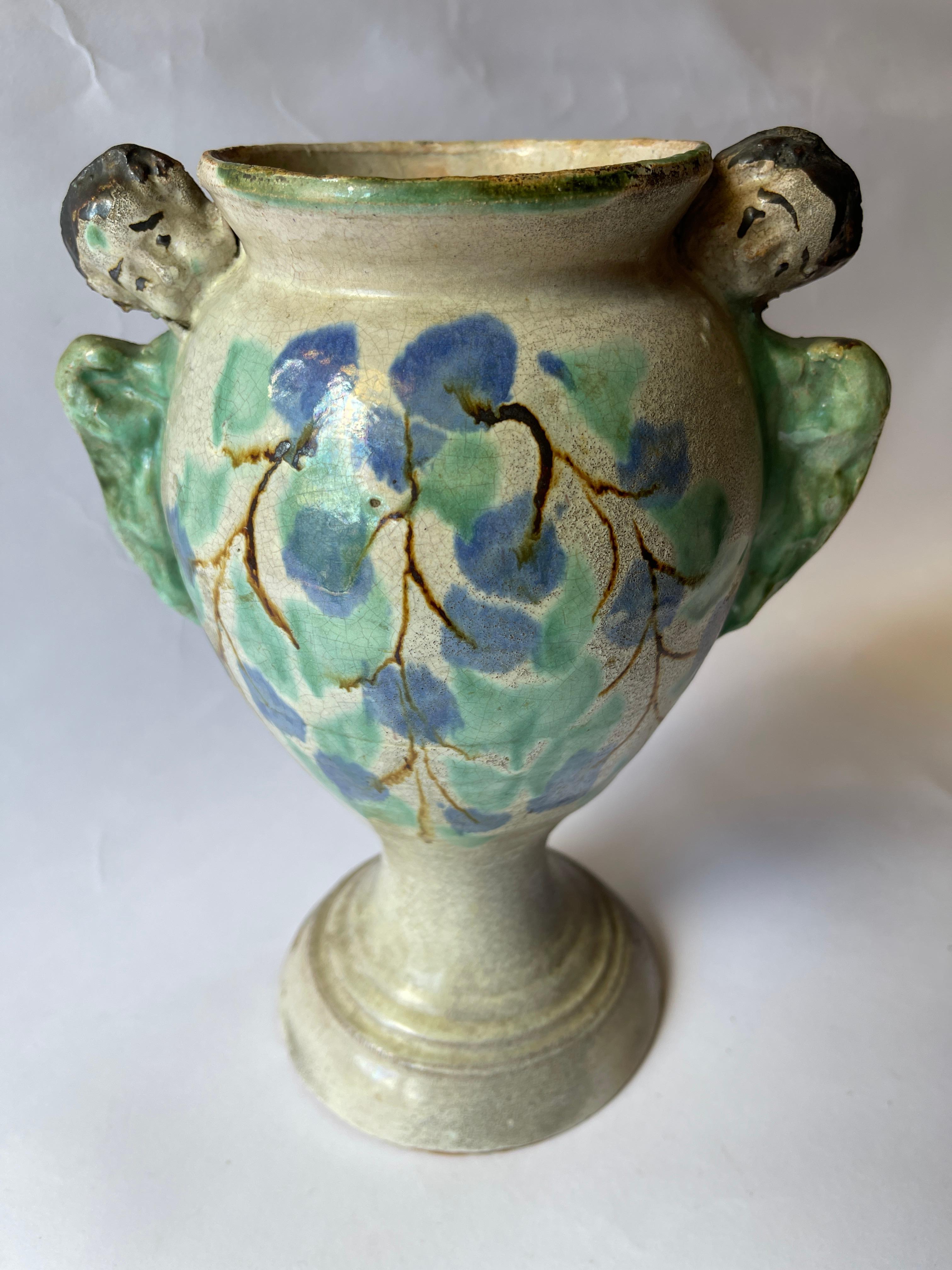 Antico vaso in maiolica coloniale spagnola, con disegno floreale dipinto a mano sul davanti. Due angeli adornano il bordo superiore, apparendo in cima a ciascun lato e scrutando le loro ali d'angelo.
Il vaso ha una bella patina, mostra i segni