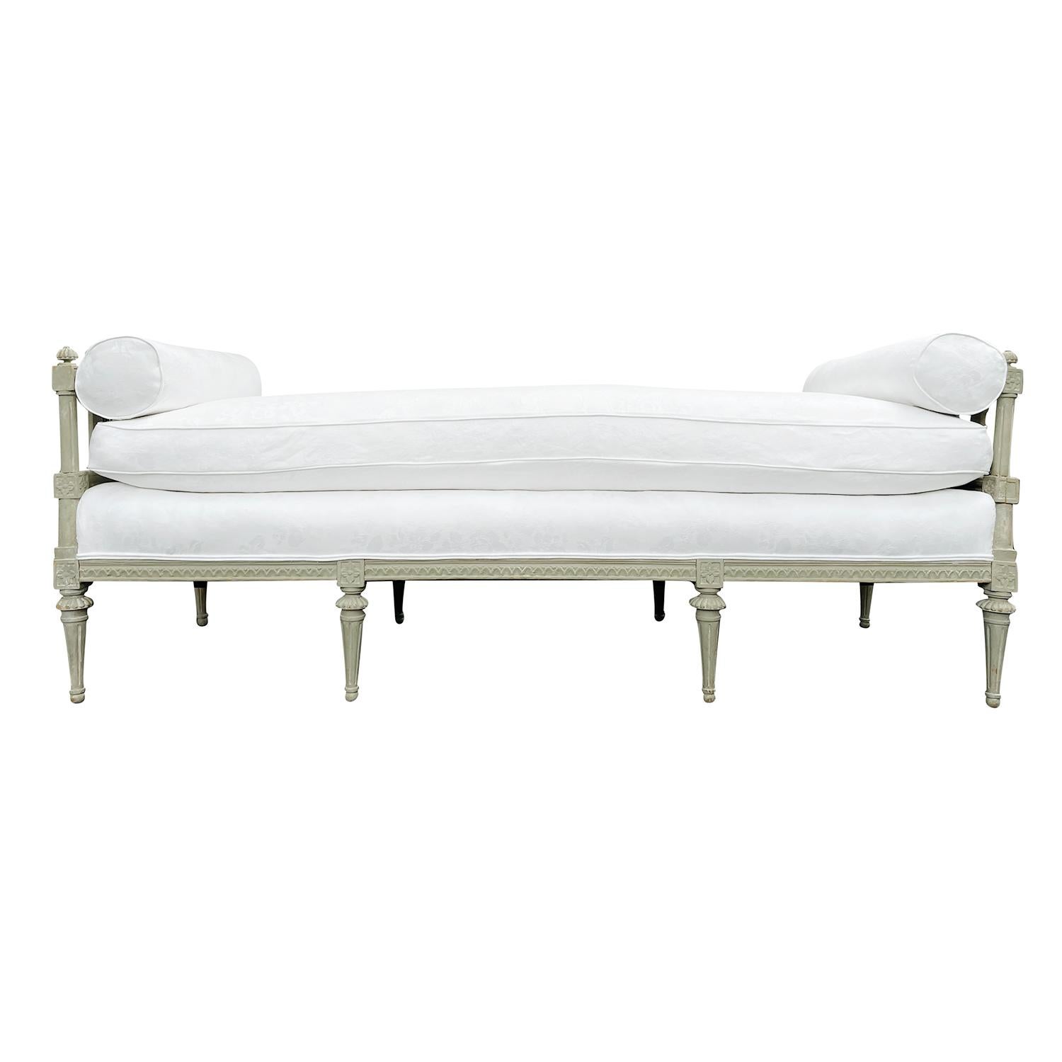 A light-grey, antique Swedish Gustavian daybed made of hand crafted painted Pinewood with two round pillows, in good condition. The sides of the Scandinavian wood sofa are spindled, supported by eight, small round tapered fluted feet, enhanced by