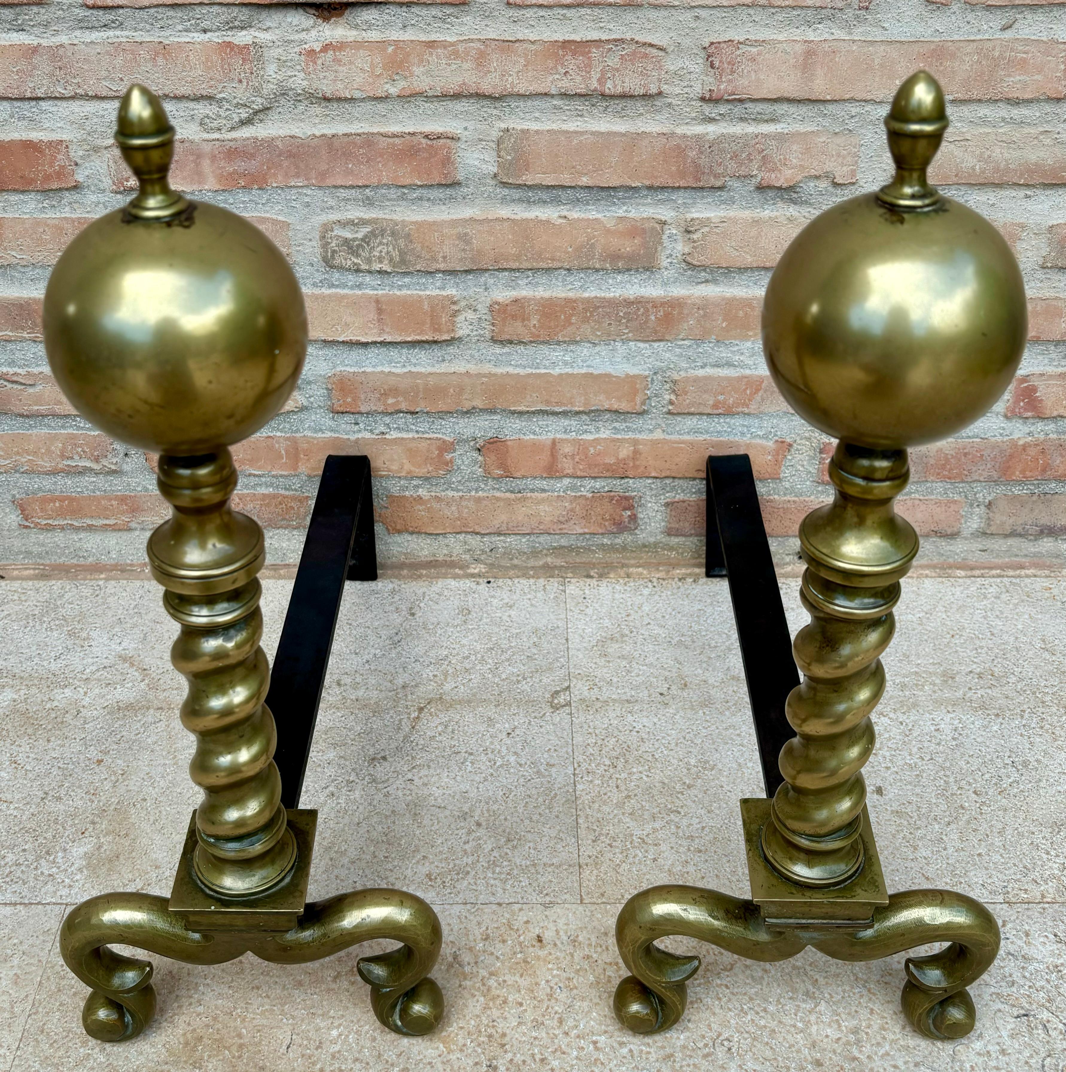 This handsome pair of fine brass Early American Chippendale andirons feature multiple turnings topped with a cannon ball style crown. The graceful spurred legs terminate on slipper feet. Sturdy log stops on the firedogs keep wood from slipping off.