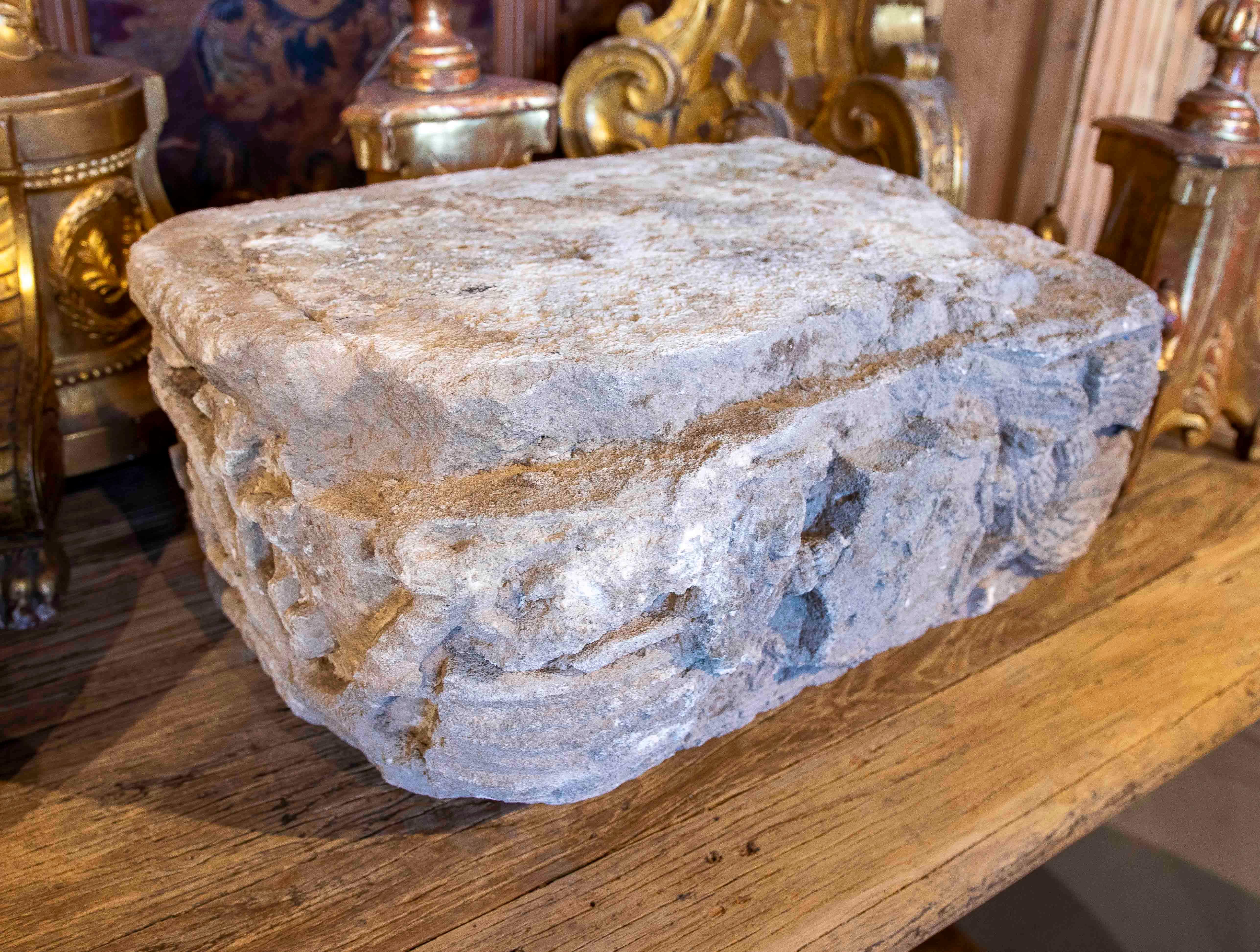 Magnífico fragmento arquitectónico antiguo en piedra tallada, de forma rectangular y con una superficie robusta que muestra signos de erosión propios del paso del tiempo. Los laterales están decorados con relieves escultóricos que, aunque