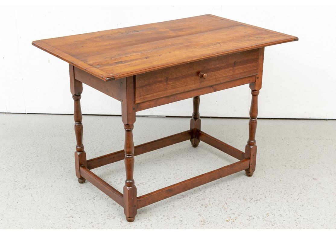 A particularly fine Tavern Table with a soft overall feel and excellent color. With a plank constructed overhanging top with dowels and bread board ends. The plain apron with one long drawer with a knob pull. Raised on turned legs with block tops