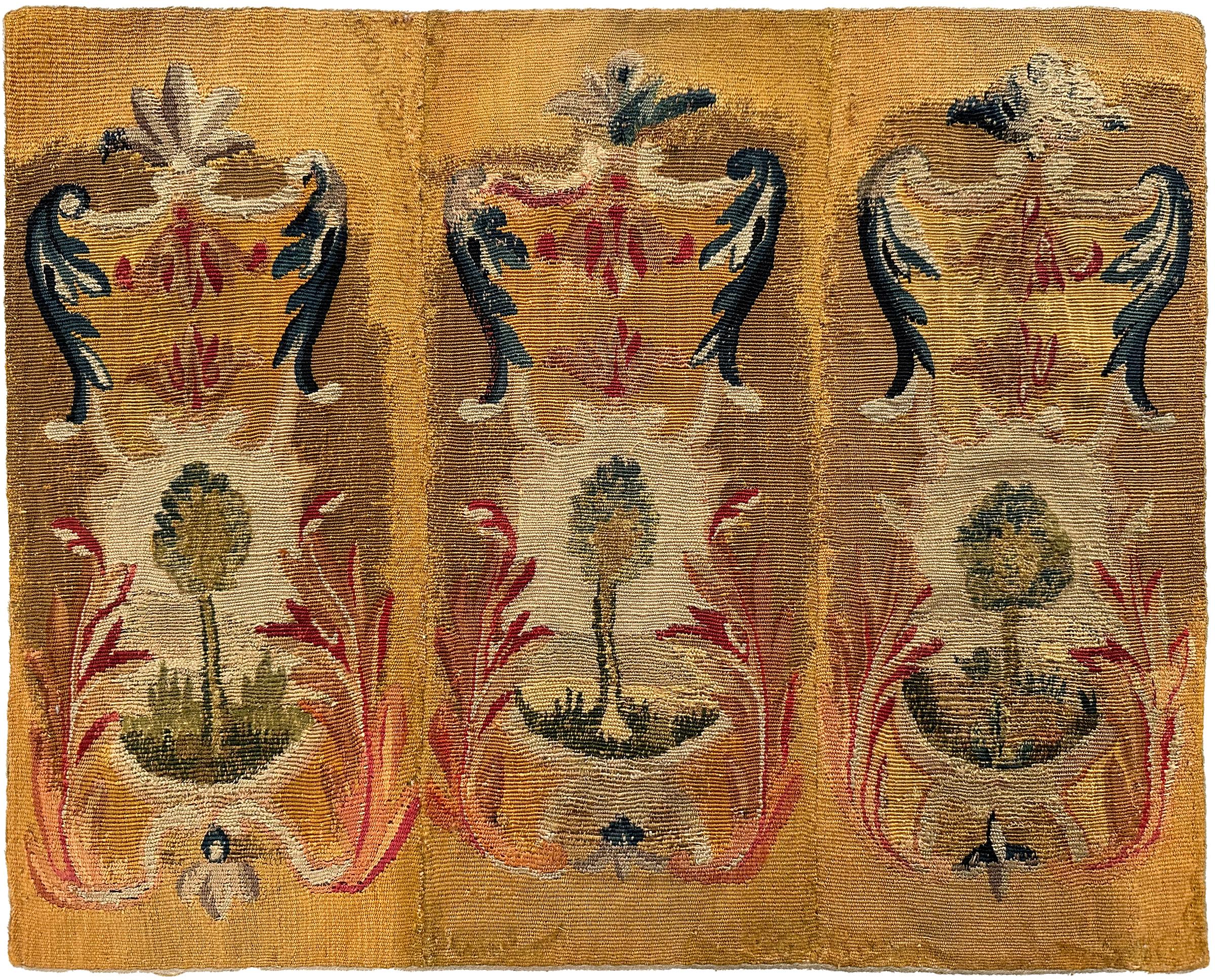 Cette tapisserie ancienne en laine et soie du XVIIIe siècle présente une composition de verdure répétitive avec des arbres stylisés encadrés par des rinceaux ornés et des motifs végétaux doux. Ses tons chauds et dorés et ses textures tissées à la