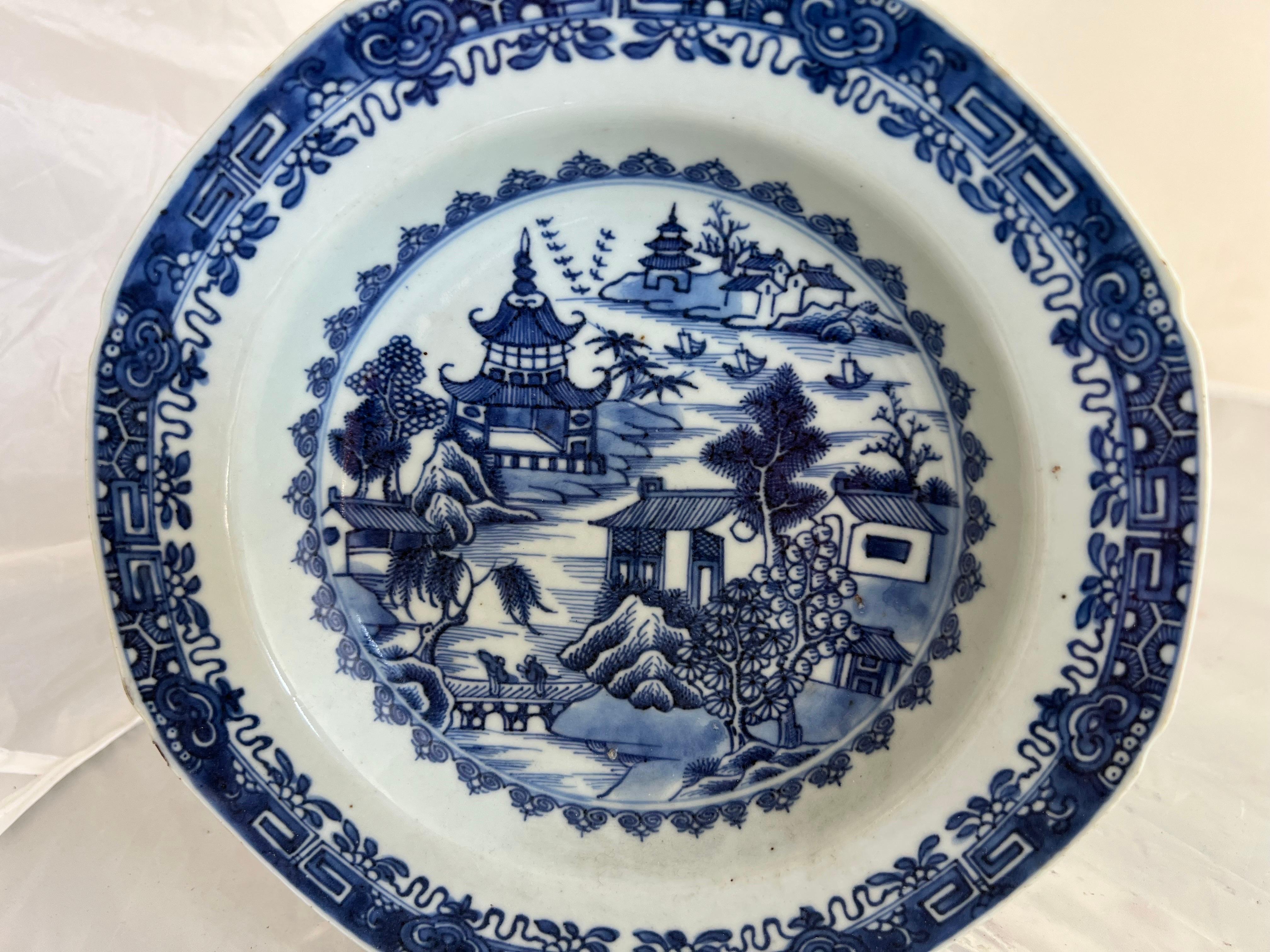 An 18th-century blue & white Chinese export plate in ironstone, depicting scenes with figures, boats, pagodas, houses, and trees, reflects the intricacy and artistry characteristic of that period.  Chinese export wares, know for their distinctive