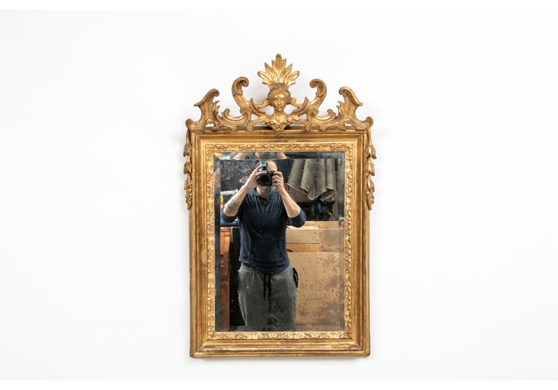Miroir mural biseauté avec double encadrement sculpté et doré. Le cimier élaboré présente un buste ailé avec une haute coiffe feuillue flanquée de feuilles d'acanthe enroulées. Les côtés supérieurs sont ornés de fleurs de clochettes sculptées.