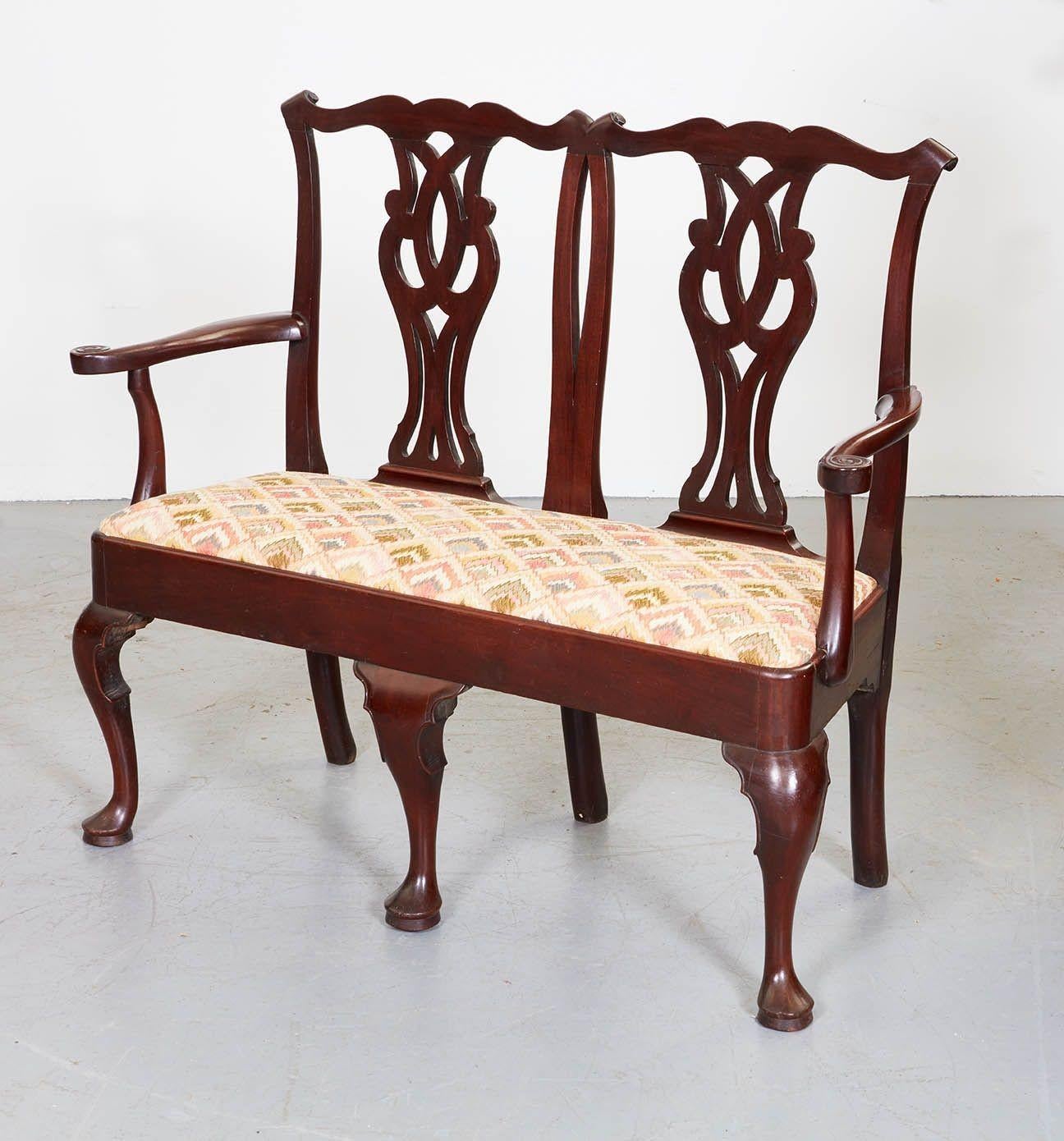 An 18th century mahogany settee having double Chippendale chair backsplats on rectangular padded seat with scrolled arms over three front cabriole legs ending in pad feet and continuous back rail legs. Later seat covering. The maker of this piece