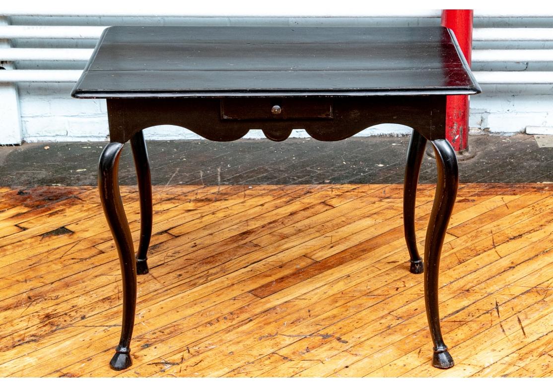 Unusual four drawer ebonized table with triple plank overhanging top with carved edge. Each side of the shaped apron with a small drawer with a ribbed knob pull. Raised on cabriole legs with cloven feet. 

Measures: 35.25” wide by 23.25 depth by