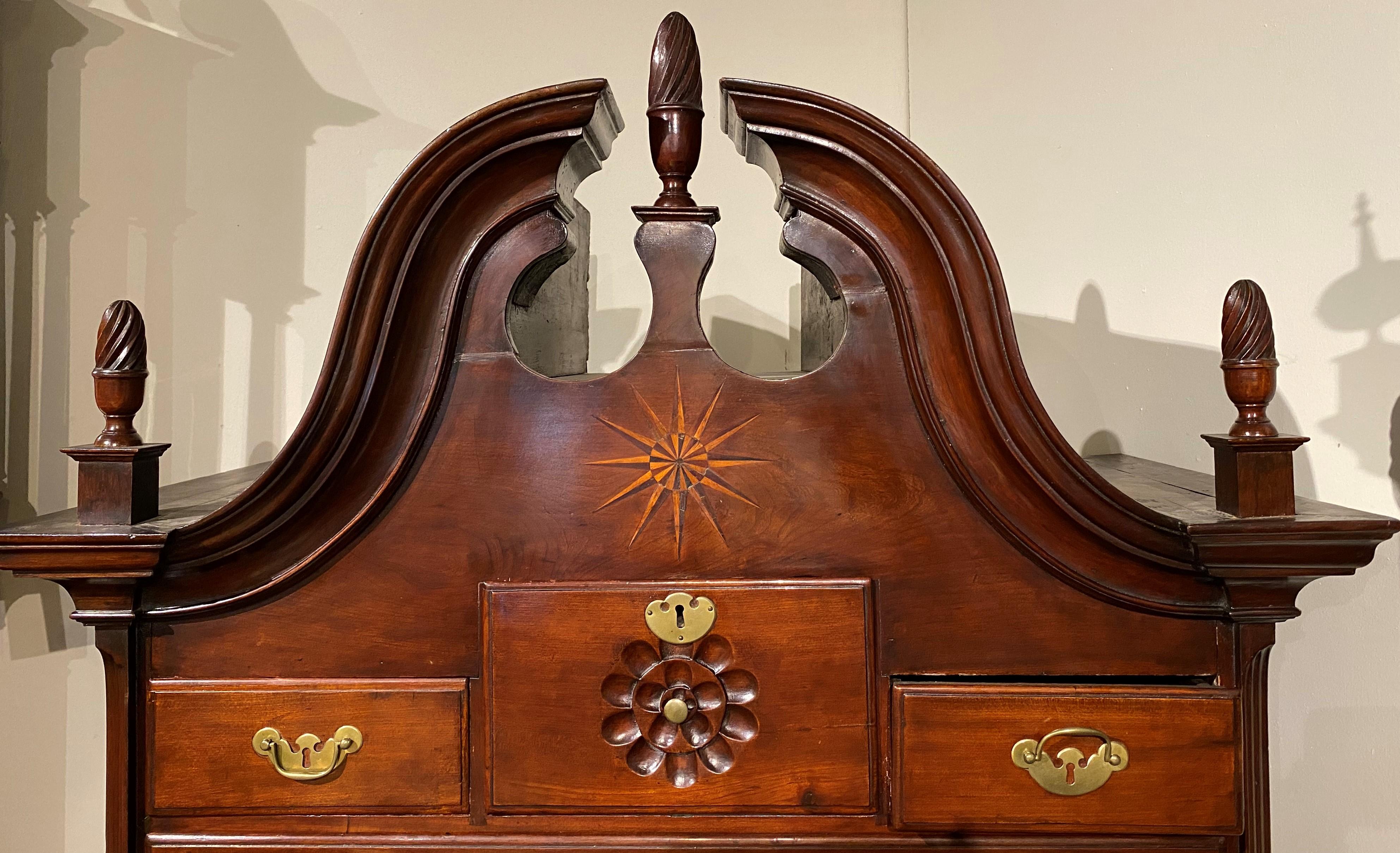 An exceptional two part Connecticut Queen Anne cherry bonnet top highboy attributed to the Workshop of Brewster Dayton, its upper case featuring a swan's neck split pediment with three carved flame finials surmounting a central inlaid star above a