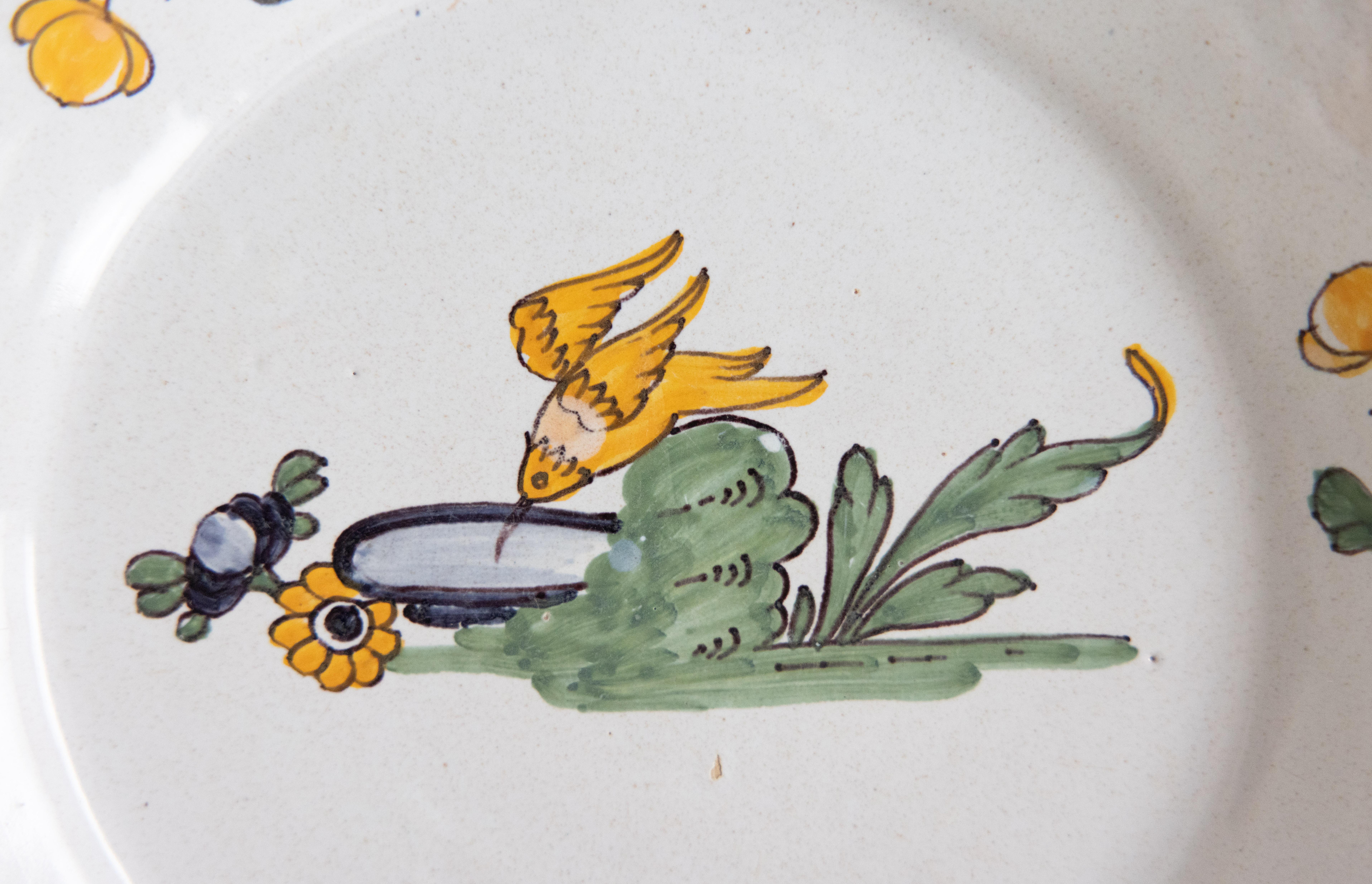 Precioso plato de loza de Nevers del siglo XVIII en el que aparece un brillante amarillo bebiendo de un baño para pájaros, con el borde decorado con flores. 