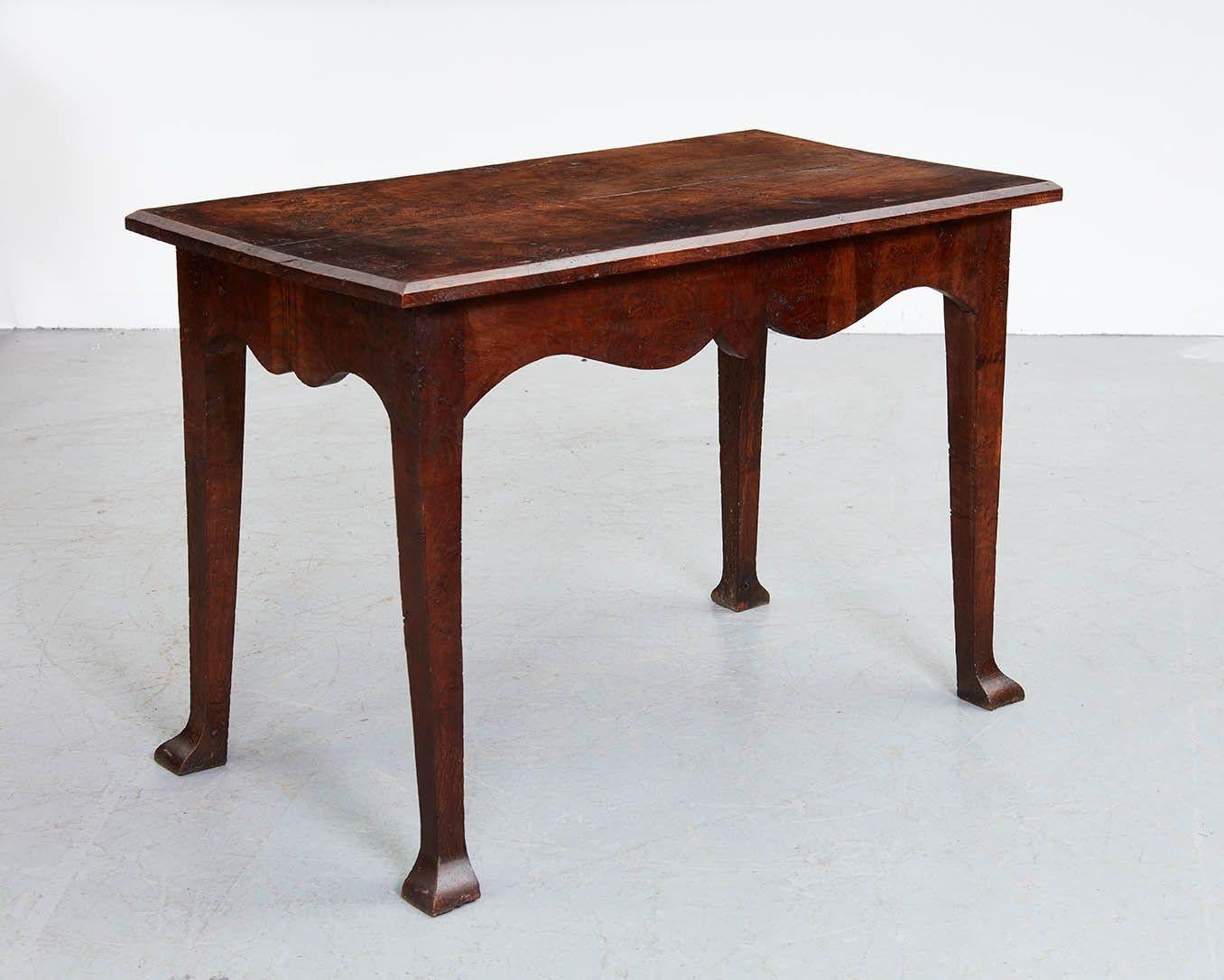 An 18th century English center table in oak having a rectangular two plank burr oak top with chamfered edges, over scalloped shaped apron all around, on tapered square section legs ending in stylized spade feet. Wonderful figuring and color, and a
