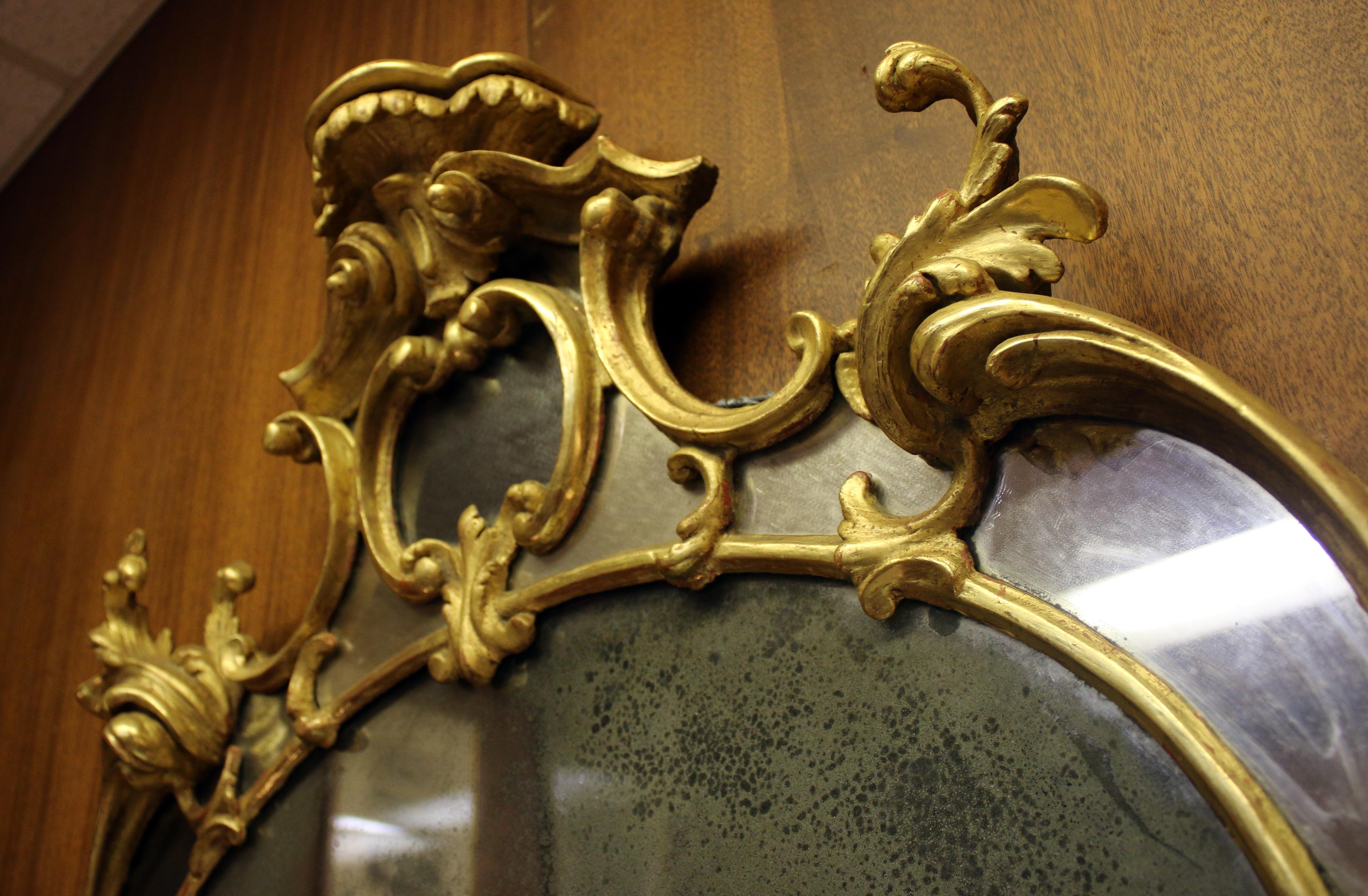 Finely carved and gilded overmantel mirror in the manner of Thomas Chippendale crested with a stylized acanthus, supported by c and s-scrolls flanking a central plate. This outstanding gold gilt wooden overmantle mirror, features three shelves. and