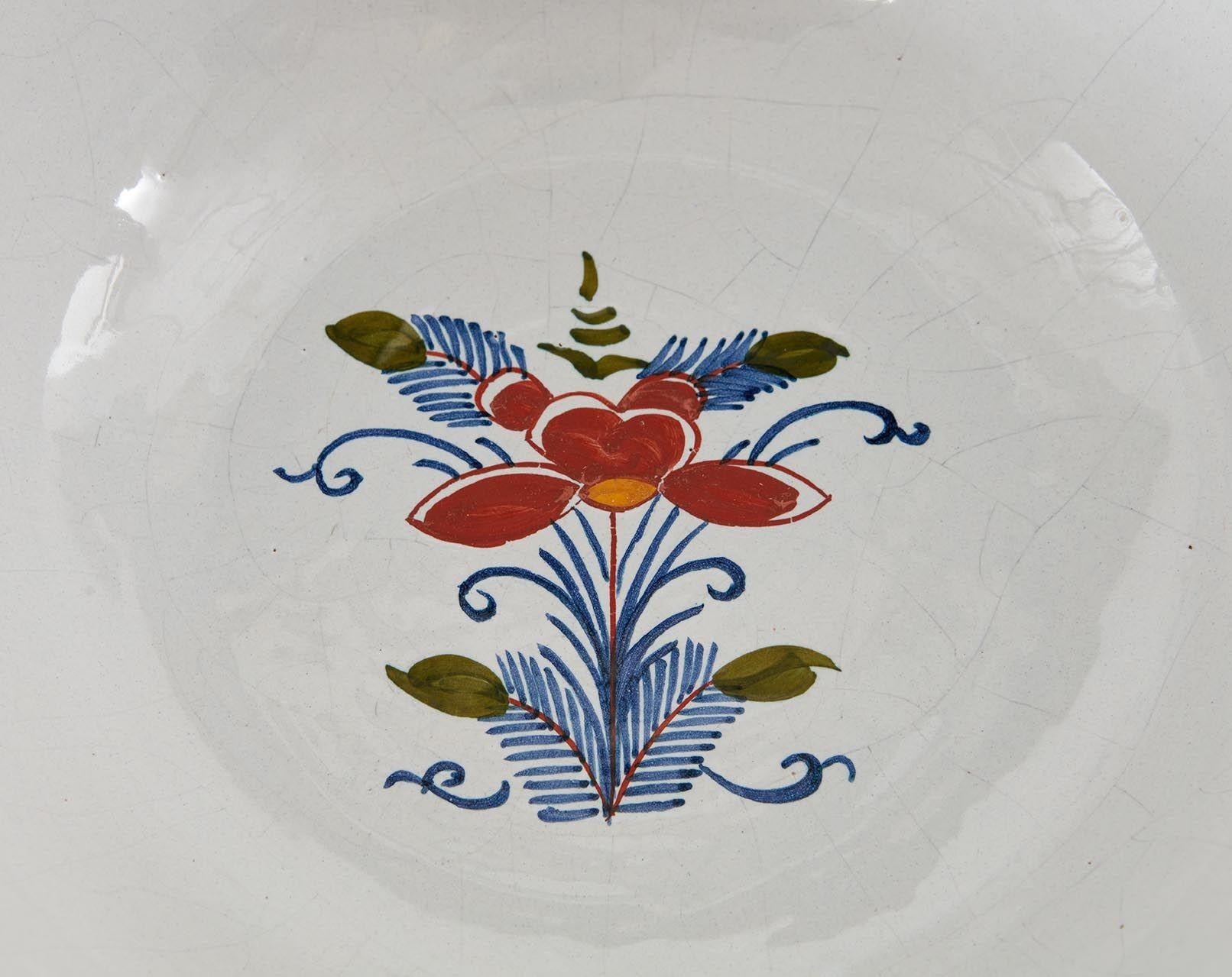 A deep delft punch bowl with polychrome decoration in reds, yellows and blues on a white ground with extensive exterior coverage depicting flowers in overlapping rounded tiles with a hatched grid above, and a single flower with leaves to the center