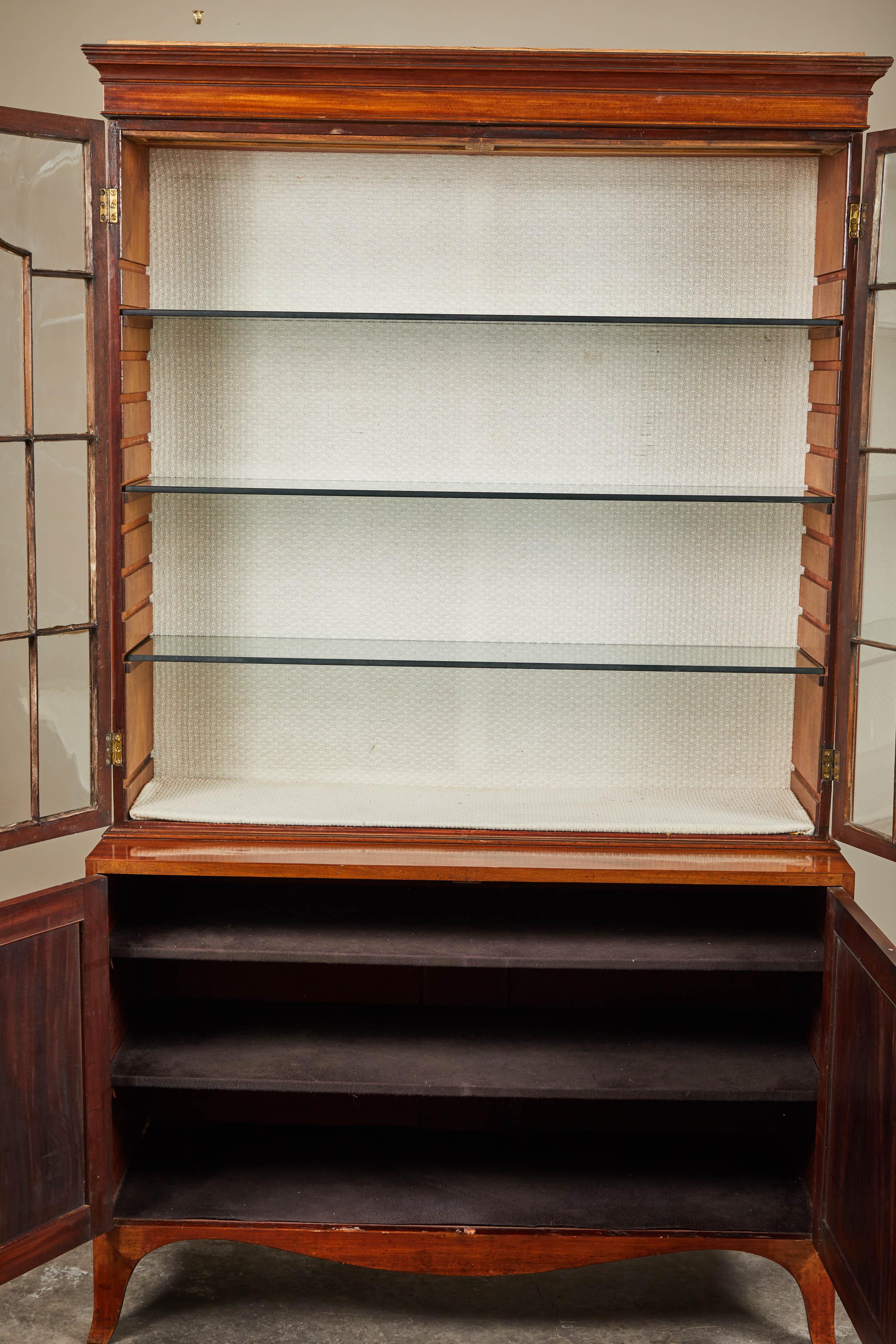 George III display cabinet. Upper section with two glass doors, lower section having two cupboard doors enclosing two lined shelves. Hidden working lights in top crown added later.