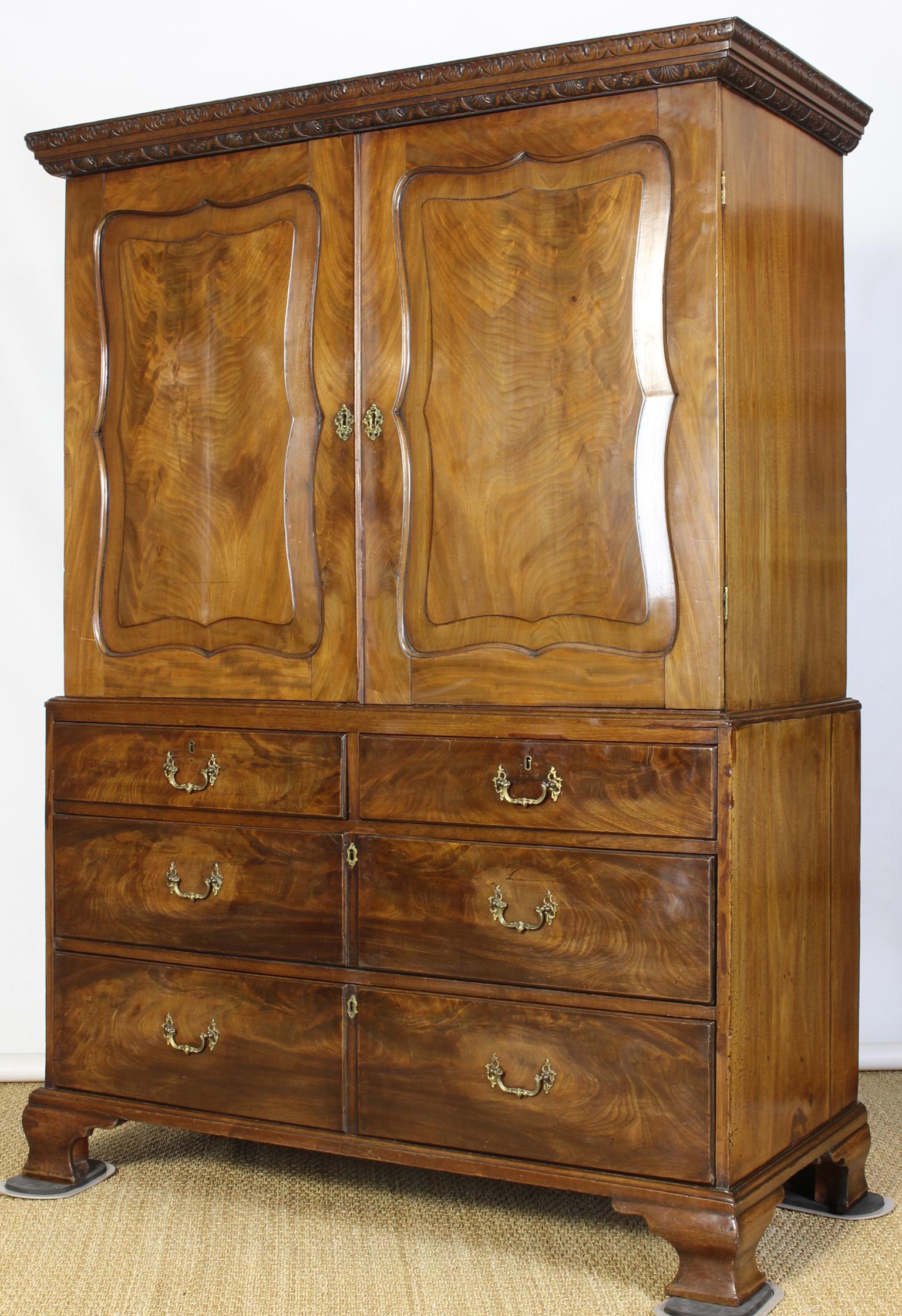 An elegant George III mahogany two part linen press with elegantly carved scalloped doors over four drawers supported on ogee bracket scroll feet.