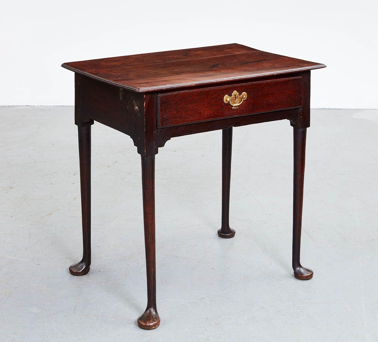 An 18th century English oak side table with two plank top having molded edge and rounded corners over single drawer with bail pull and brass back plate, having front apron with notched center, corner brackets at leg joins, and standing on tall
