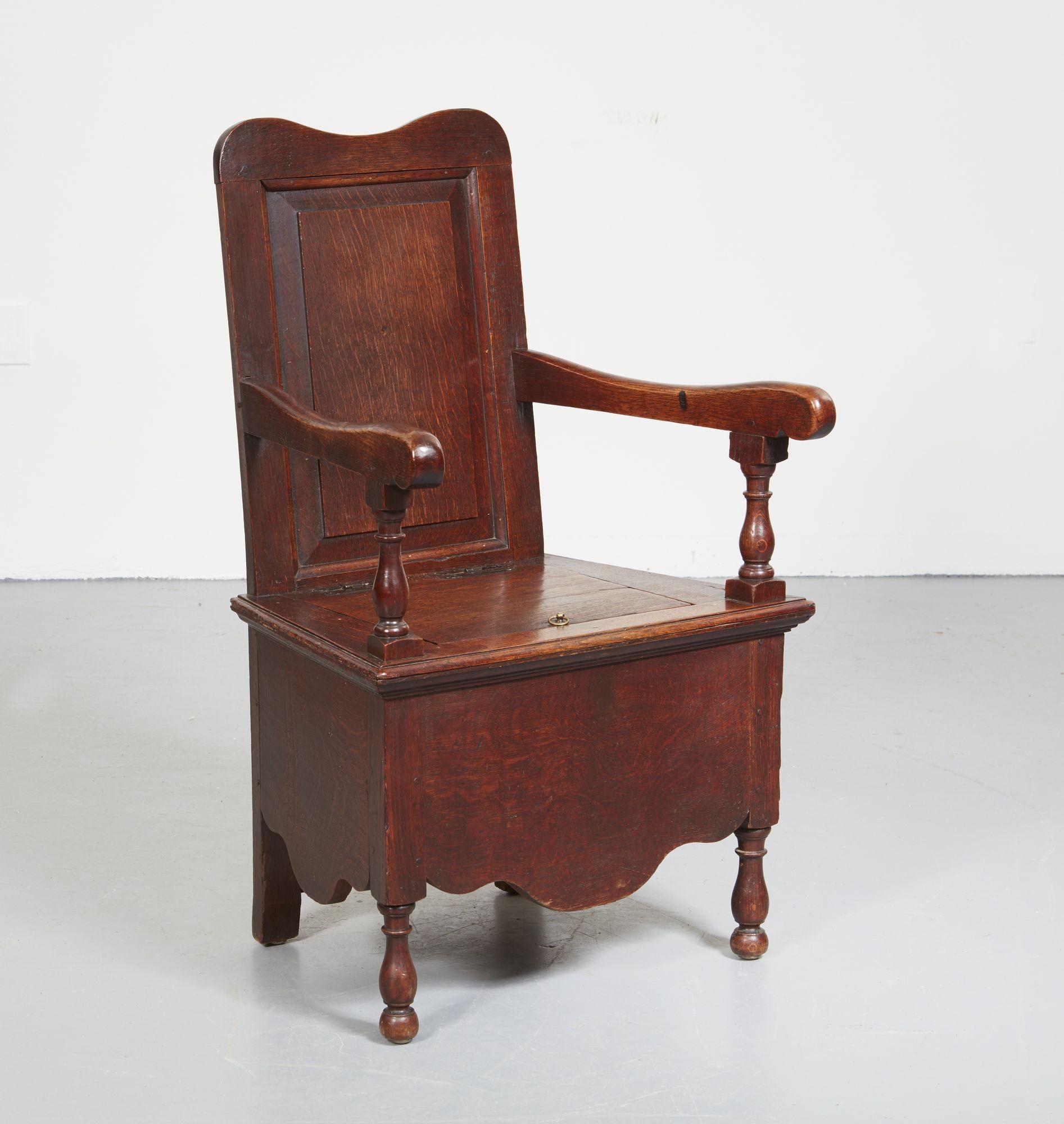 An 18th century oak commode armchair having solid back with reverse arched and central rectangular inset panel, solid sides and base with shaped aprons, over open curved arms on turned supports, lift top seat and standing on turned legs. Original
