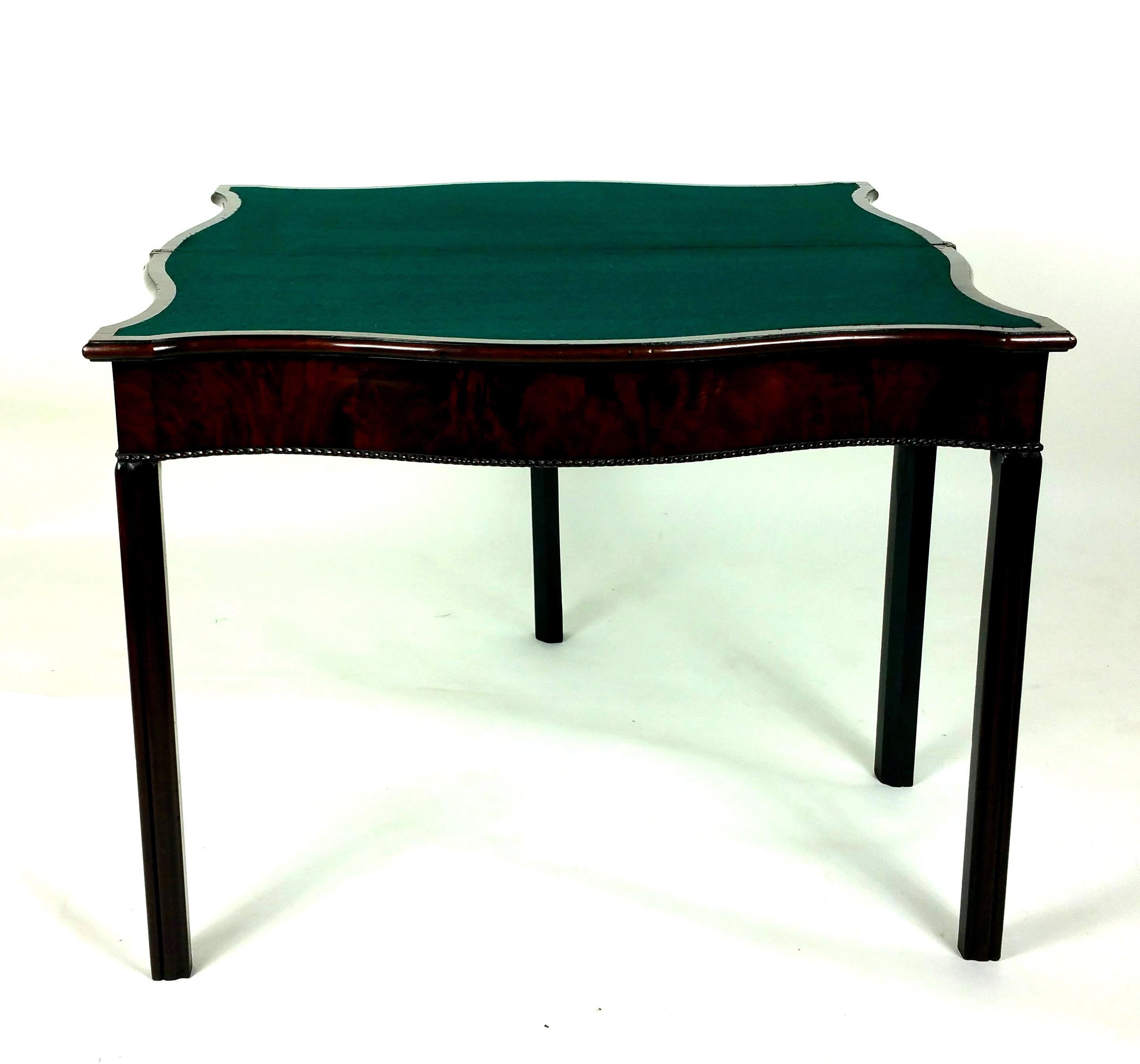 This lovely 18th century figured mahogany serpentine shaped card table that stands on moulded chamfered supports and has a fold over design which, when opened reveals a green baize lined interior. It measures 28 in – 71.1 cm in height and 18 ½ in –