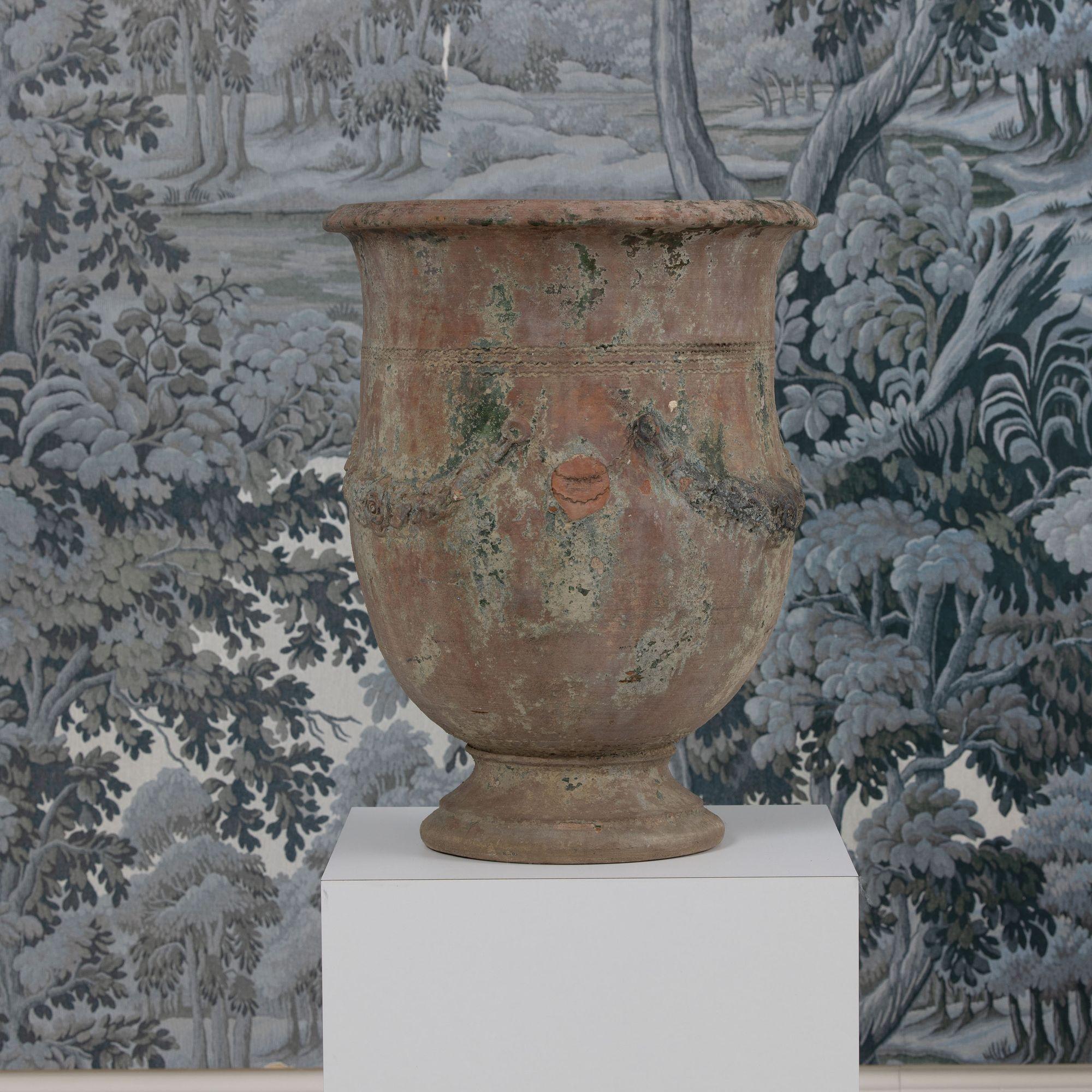 Jardiniere Anduze en terre cuite de taille inhabituelle. Une trouvaille rare. Cette pièce présente une belle glaçure usée de couleur verte et ocre délavée avec des guirlandes traditionnelles en relief. Le pot est typiquement ébréché, ce qui renforce