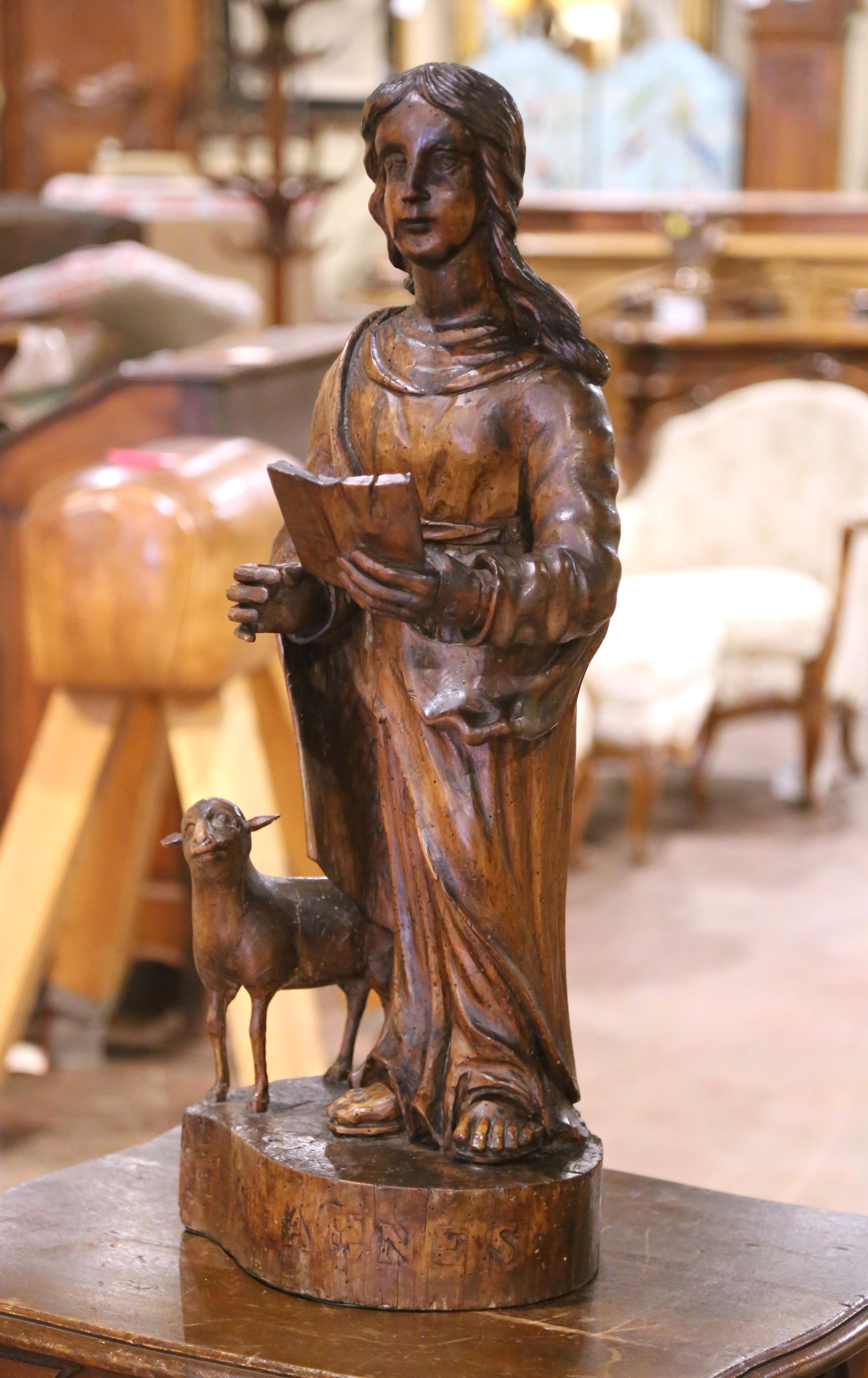 This evocative sculpture, hand-carved in France circa 1780 from solid walnut, depicts Saint John the Baptist, shown in youthful form holding an open book and accompanied by a lamb—his traditional attribute as the herald of Christ. The figure stands