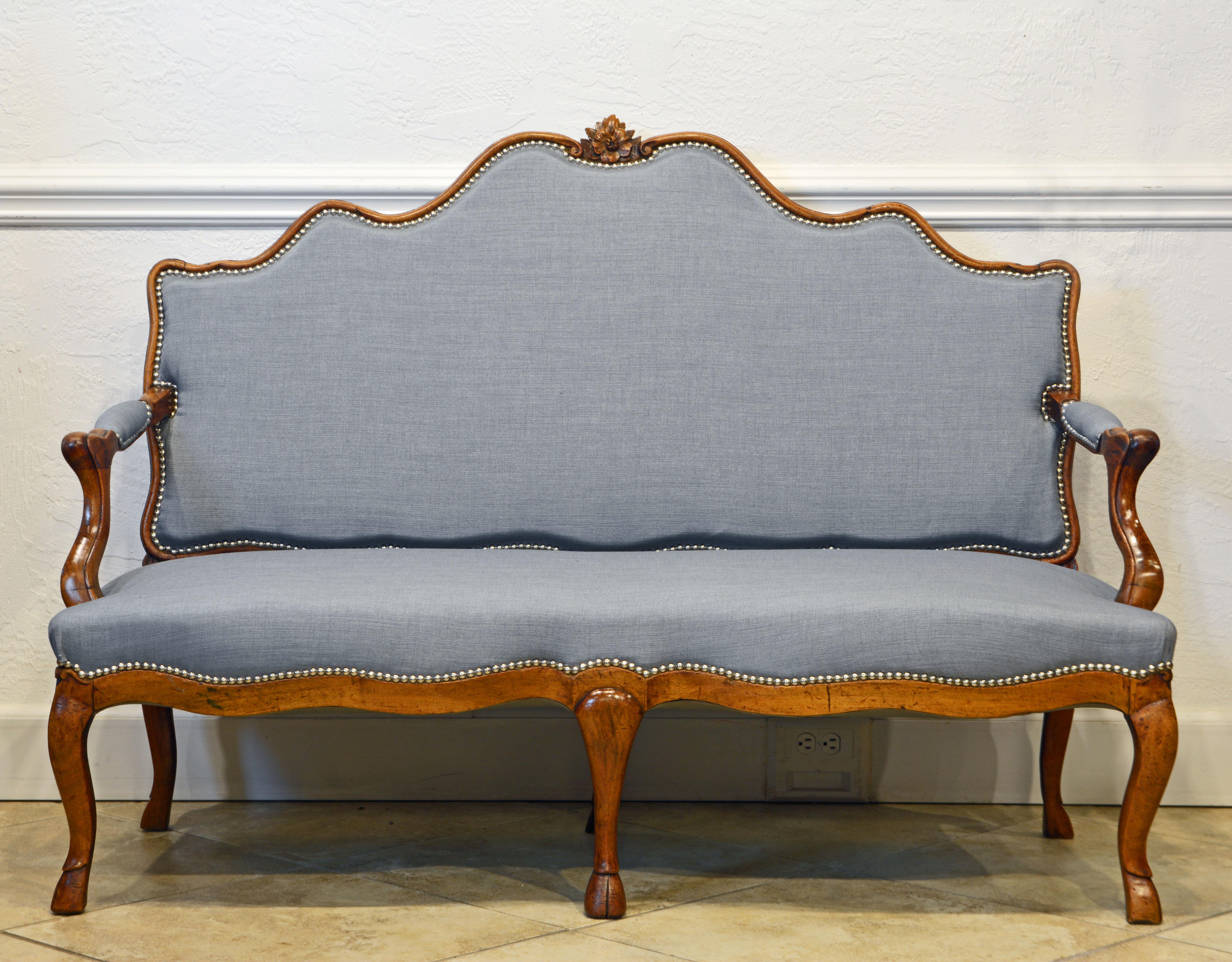 This shapely French Louis XV canapé or settee feature a carved padded serpentine back, partly padded scrolled arm rests and an upholstered seat with scalloped apron resting on six well carved cabriole legs ending in hoof feet, 18th century. This