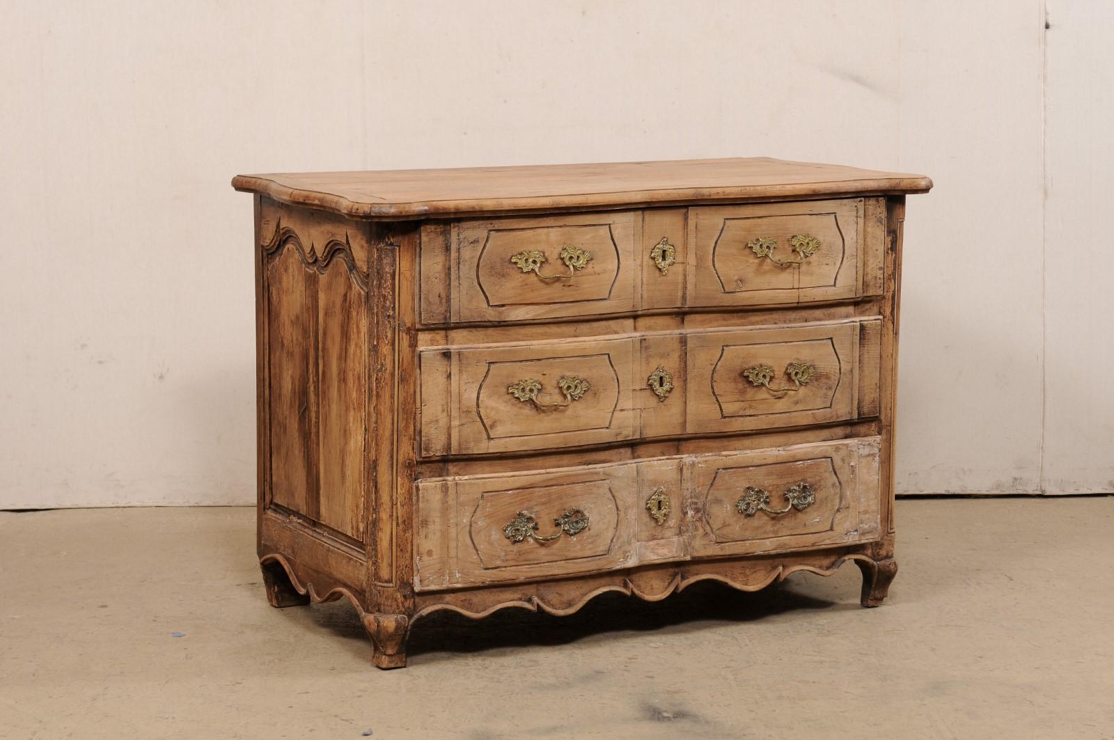A French Louis XV carved-wood commode, with subtle serpentine front, from the 18th century. This antique chest from France has a shapely top with scalloped sides and serpentine front, carved to mimic the shape of the case below, which houses three