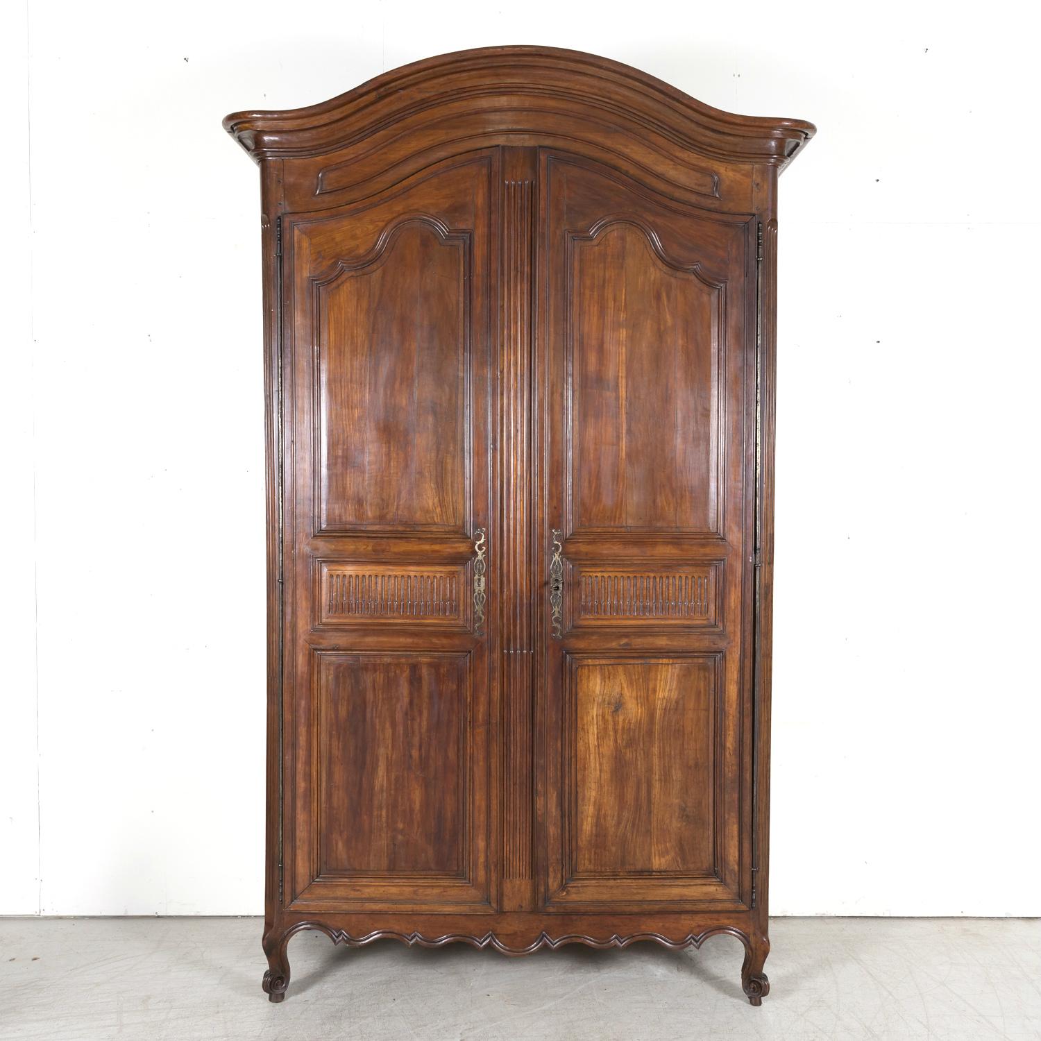 A monumental 18th century French Louis XV-Louis XVI Transition period solid walnut chateau armoire handcrafted by skilled artisans from the Bordeaux region of France, circa 1750s, having a chapeau de gendarme crown sitting atop a hand carved frieze.