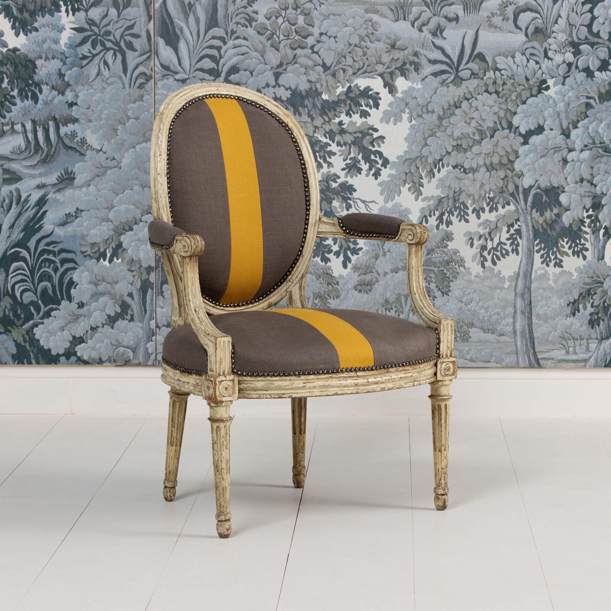 A French armchair from the Louis XVI period in original paint and newly upholstered in two fabrics with studs, circa 1790. Channeled frame, with oval, cushion backrest. Shaped arms with elbow cushions. A generous, comfortable seat with bowed apron