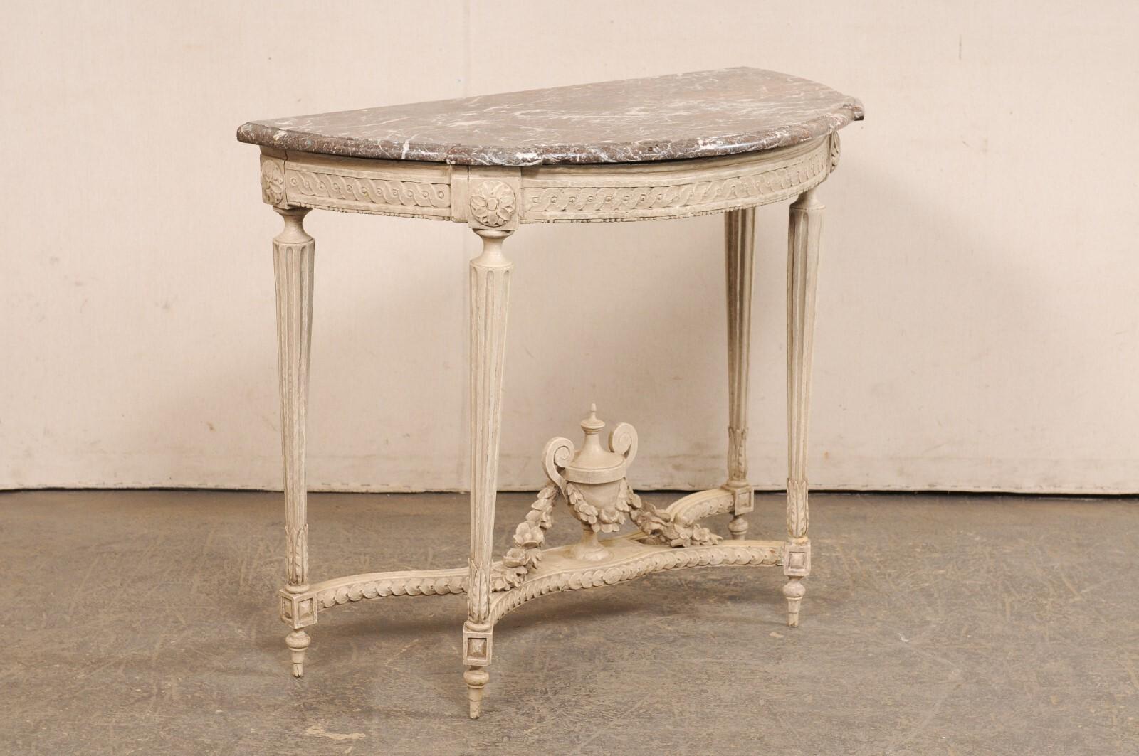 A French Neoclassical period nicely-carved demi lune console table, with its original marble top and carved urn finial accent at underside, from the 18th century. This antique table from France features its original half-circular/demi shaped marble