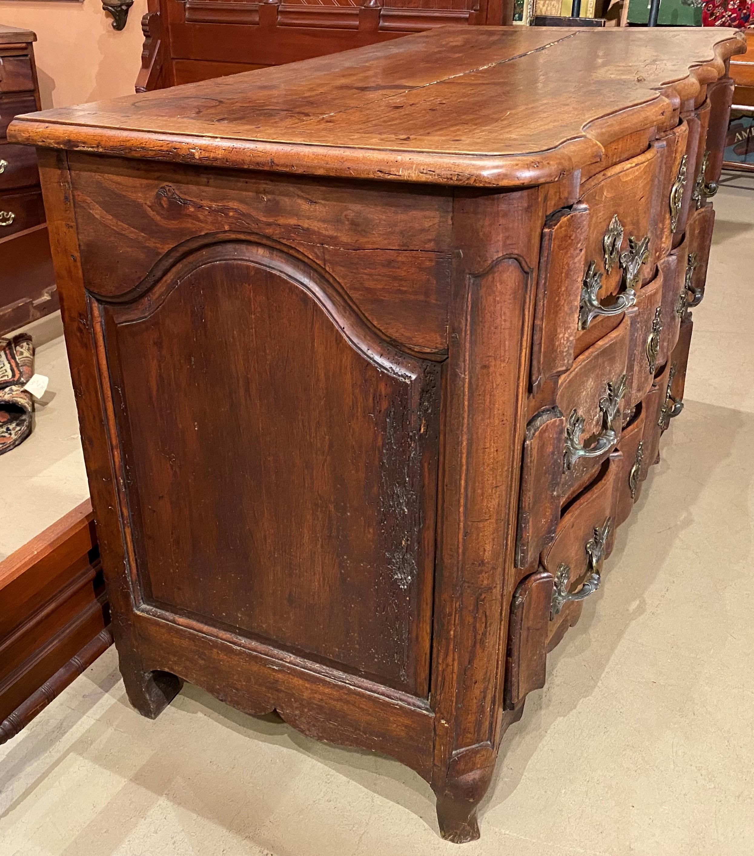 A wonderful French Provincial walnut commode with serpentine front and conforming molded edge top, surmounting three fitted top drawers (one of which is hidden in the center), over two additional long drawers, all with original bold foliate bronze
