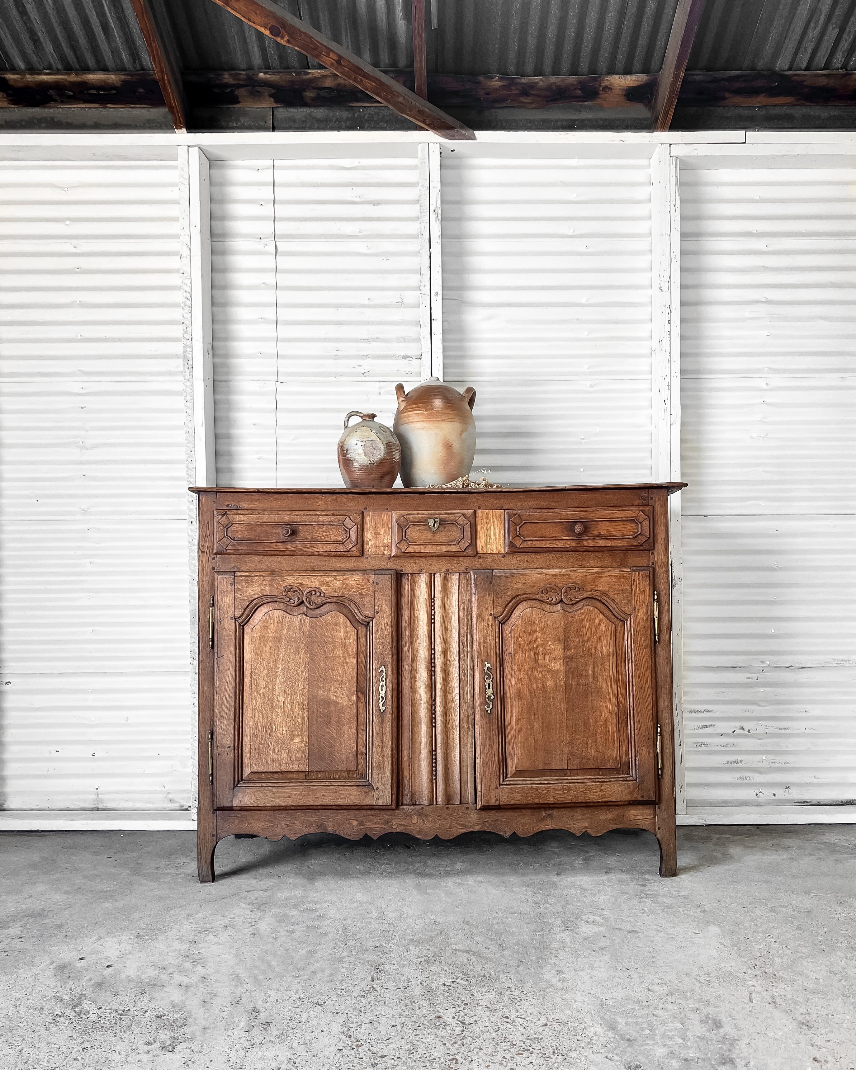 Antique French country sideboard dating to the mid-18th century has three drawers over two carved paneled doors that open to reveal a single shelf. Constructed from oak with a beautiful warm, aged patina, the sideboard features a planked top, a