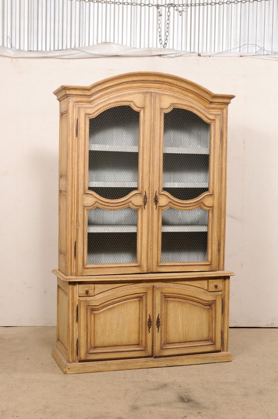 A French Rococo tall wooden display and storage cabinet from the 18th century. This antique oak wood cabinet from France features a nicely arched and molded center top pediment, is designed throughout in nice molding & raised panels, and presented