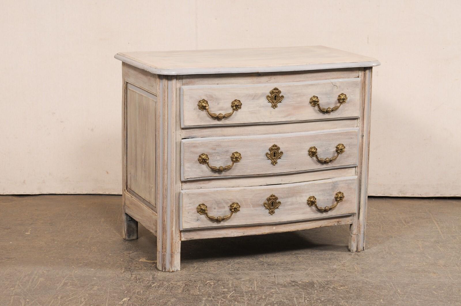 A French painted wood serpentine commode, with gorgeous brass hardware, from the 18th century. This antique chest from France has a very softly curved serpentine design at front, which is carried from the top and down the along the three drawers.
