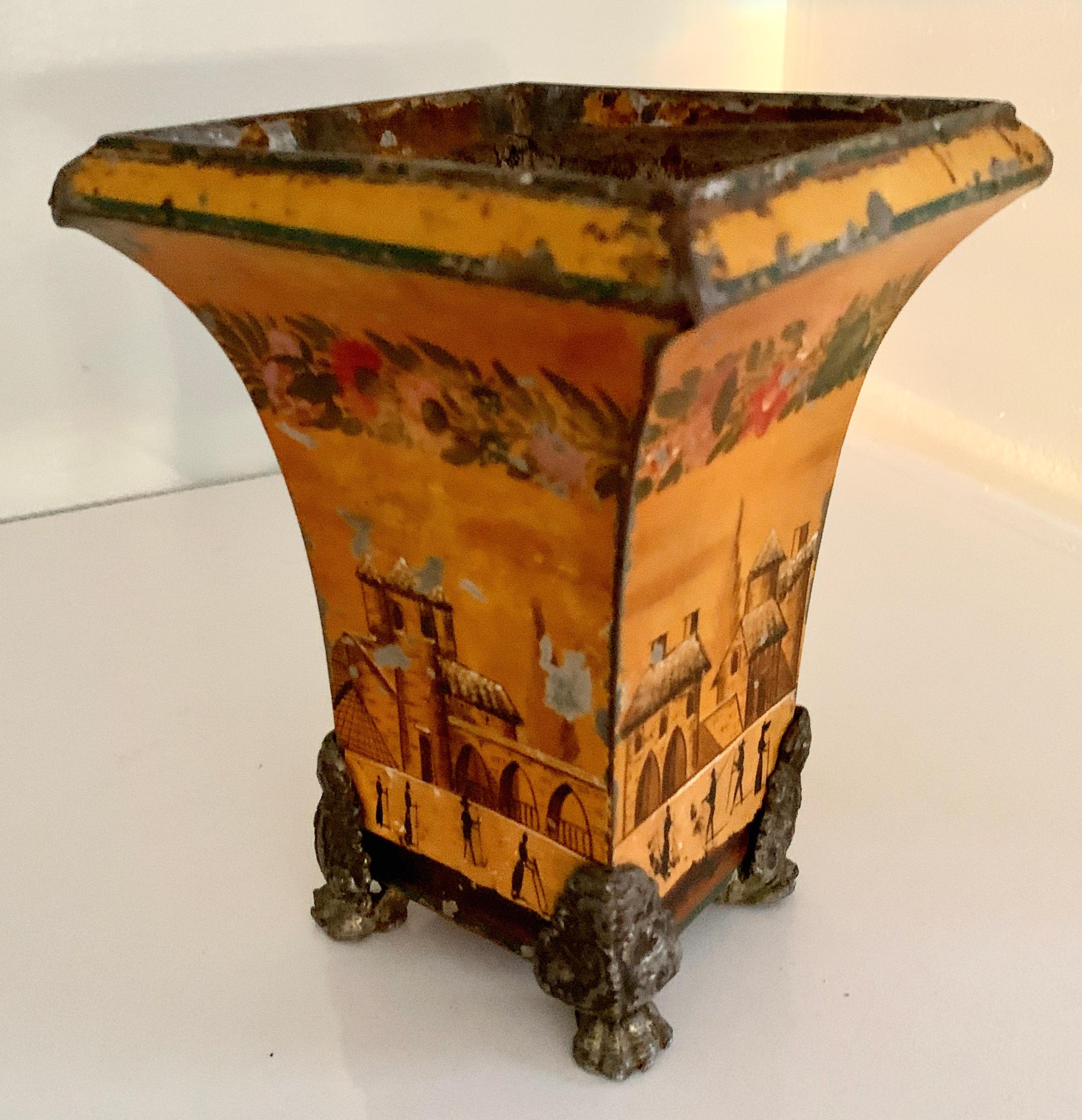 A yellow tole planter with village style scene with claw feet. The piece has a removable liner. A compliment to any table or shelf - A plate or under will need to be used as the liner and planter do have some areas that leak, (only mildly) - perfect