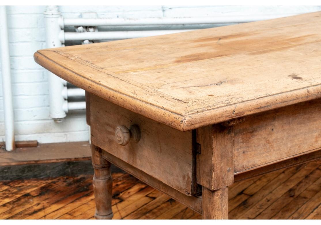 A large early rectangular table with overhanging banded plank constructed top. (the top with old crack fills, see photos). With an apron drawer near one end, and another drawer on one short end. Raised on heavy carved turned legs. With nice