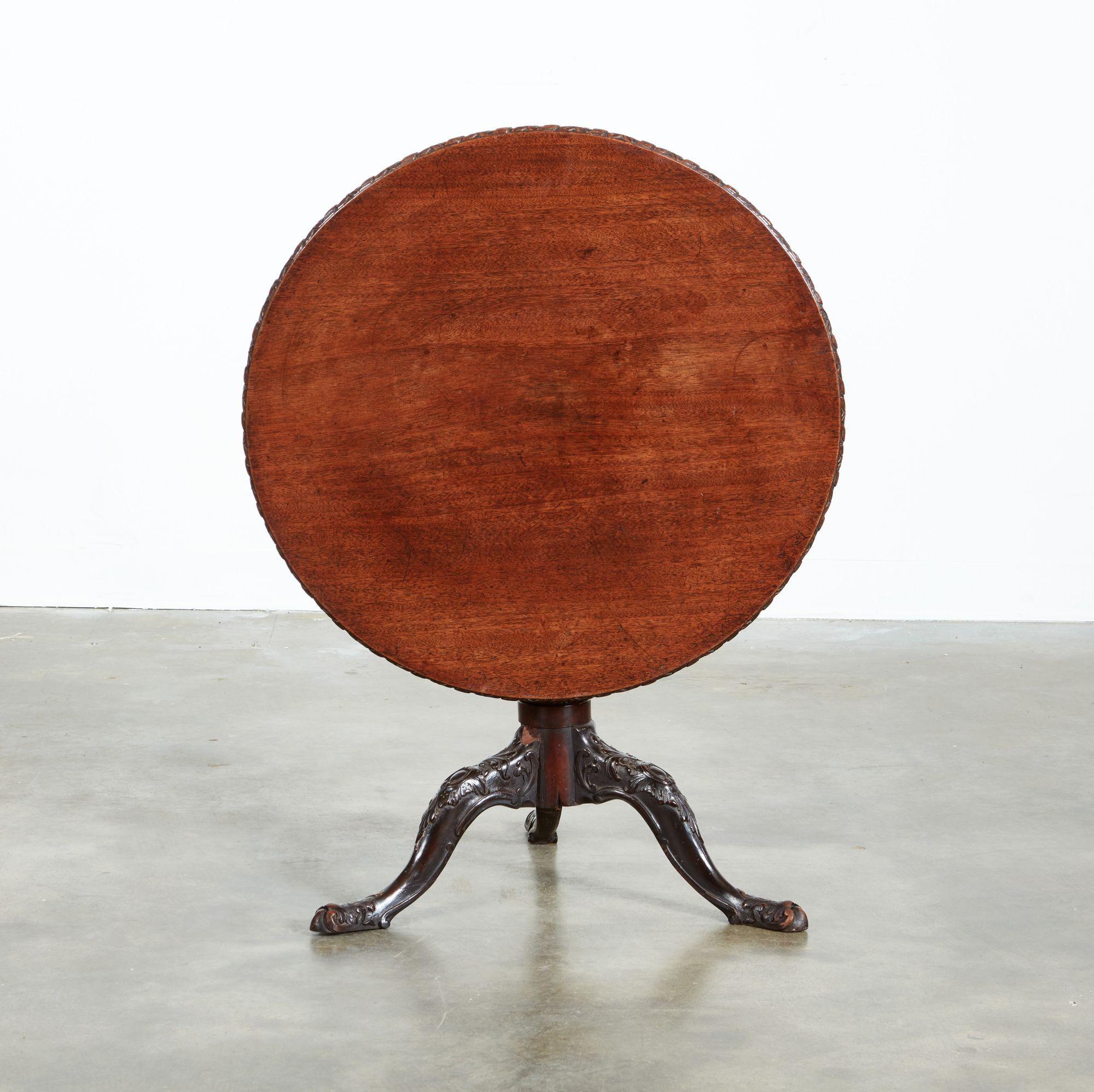 George II tilt top low tea table, the single plank padouk top with heavily carved edge, over balustrade turned shaft with spiral fluting and standing on rococo carved legs with foliate and cabochon carving, all with good rich color and patination.