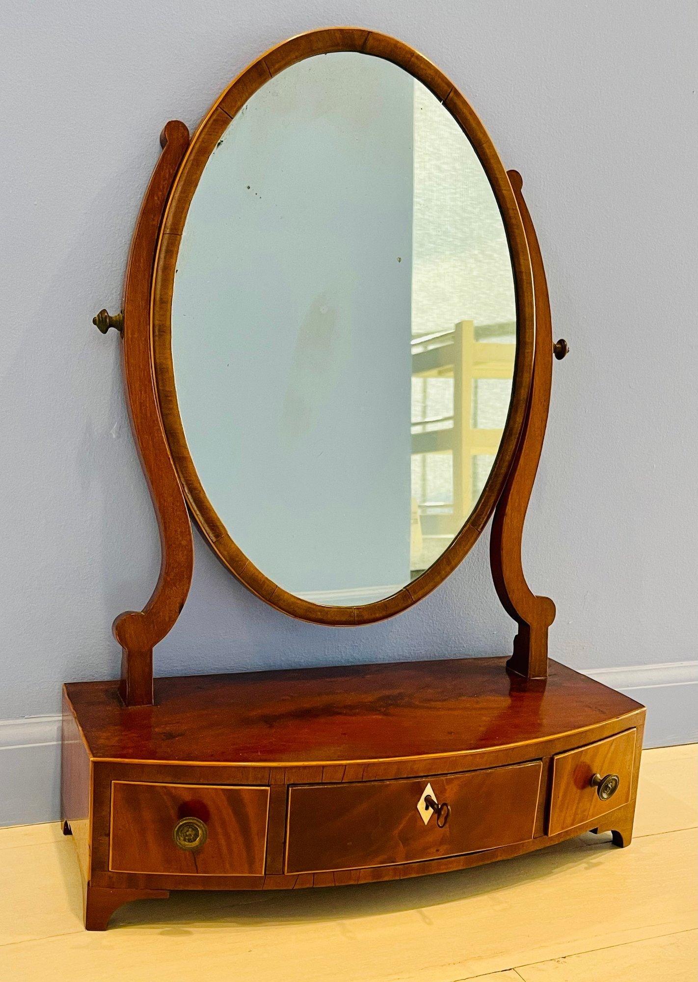 A rare and very good quality Georgian Mahogany dressing and shaving tilting oval mounted mirror. Above a bow front case with 3 drawers raised on splay feet. Brass handles & keyhole escutcheon. Key is included.

24