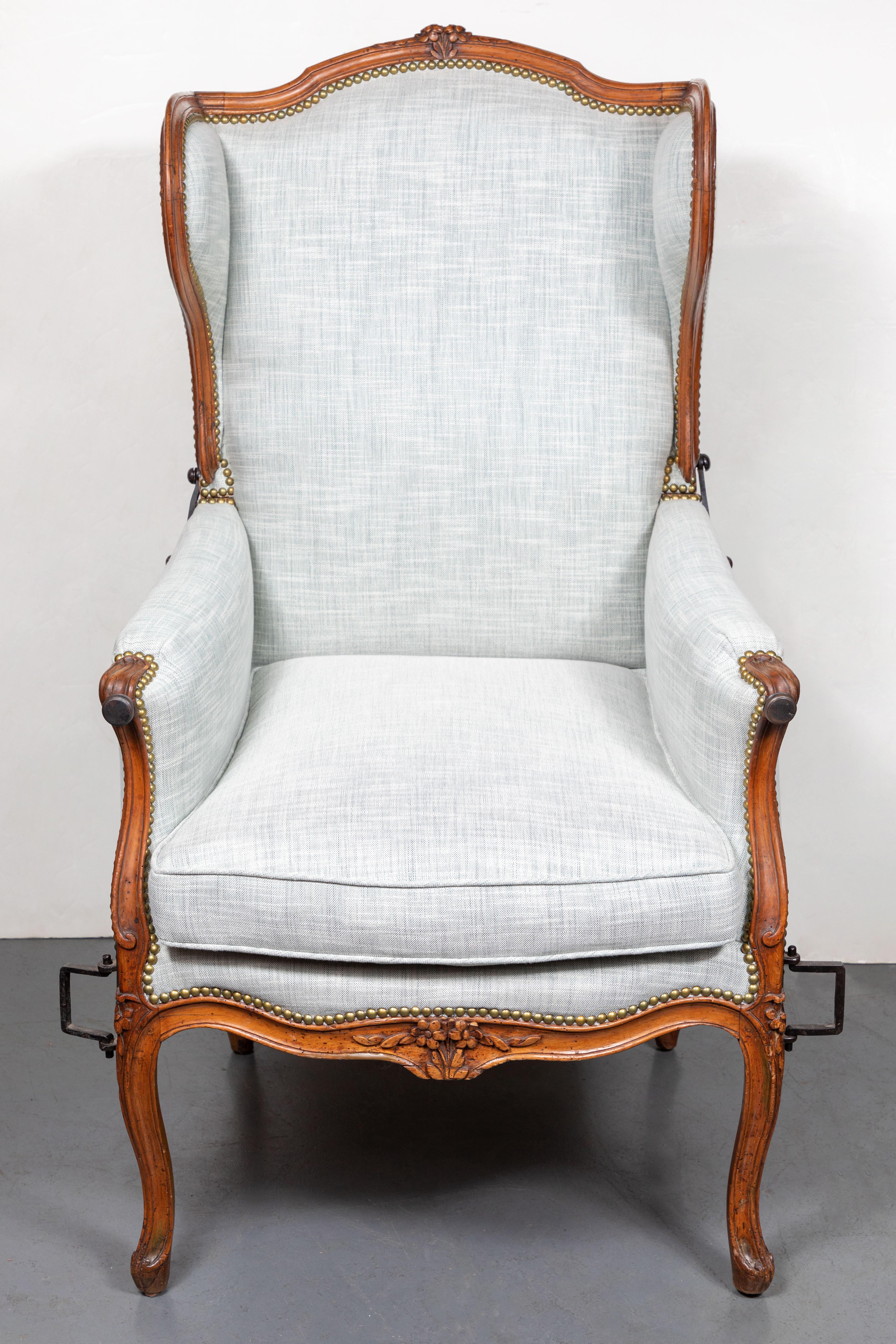 Hand carved beechwood, reclining, wing-back invalide chair in wonderful working condition. The frame fit with hand-forged, wrought iron handles and toothed arc to specify chair back angle. The frame upholstered in new fabric with brass nail heads,