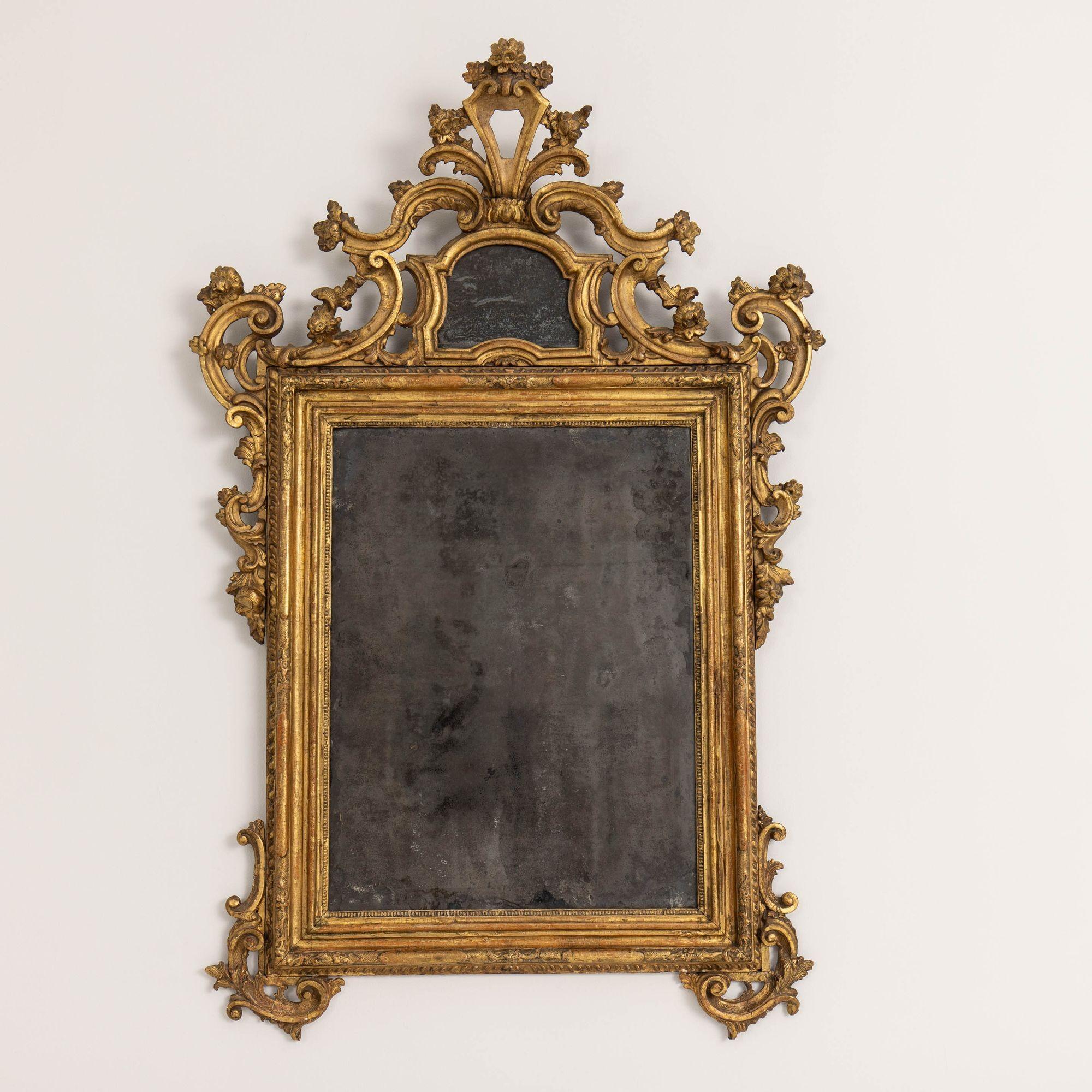 Squisita specchiera veneziana del XVIII secolo di epoca barocca con piatti originali in legno dorato e mercurio splendidamente invecchiati, 1740 circa. Si erge su due piedi a voluta con motivi a voluta finemente intagliati e traforati di fiori e