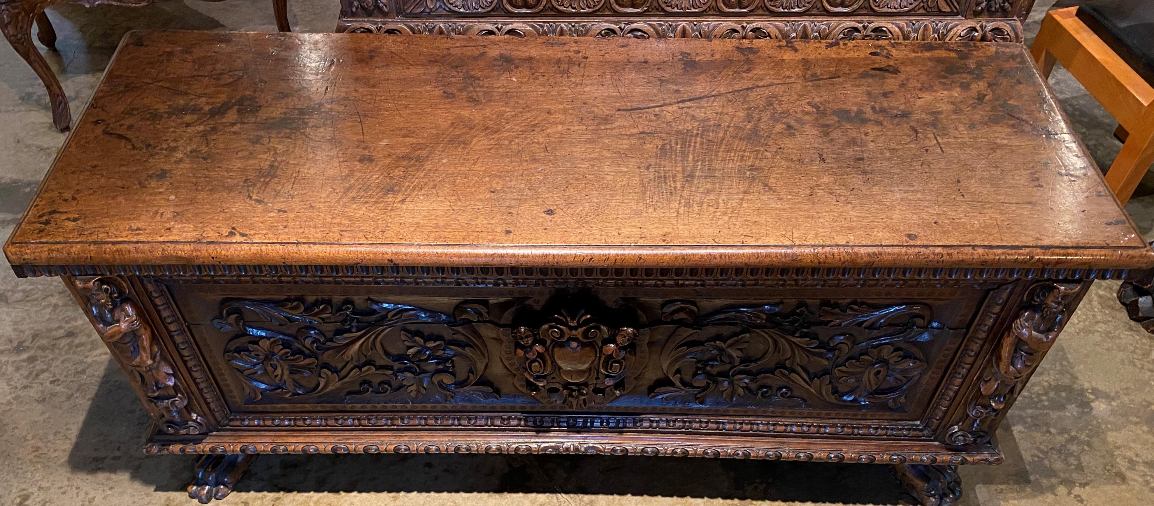 A finely carved Baroque style oak cassone with corner full figures, center cartouche with additional relief carved figures flanked by scrolled foliate relief carving, gadrooned edges on hinged top and case, original iron strap hinges and hardware,